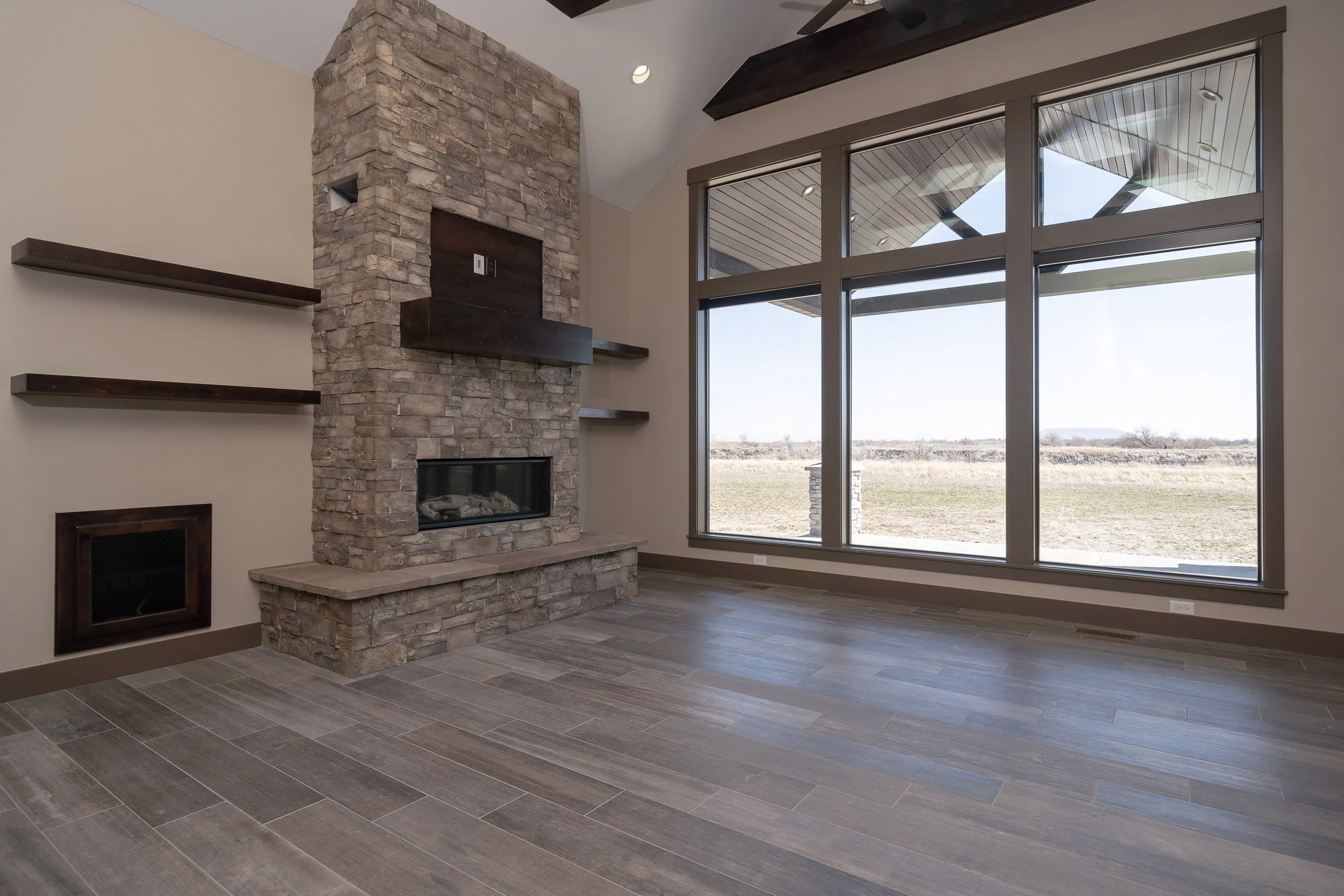 Living room with a tall stone fireplace and large windows — JAB Construction’s Stone Craftsman custom home in Roberts, Idaho.