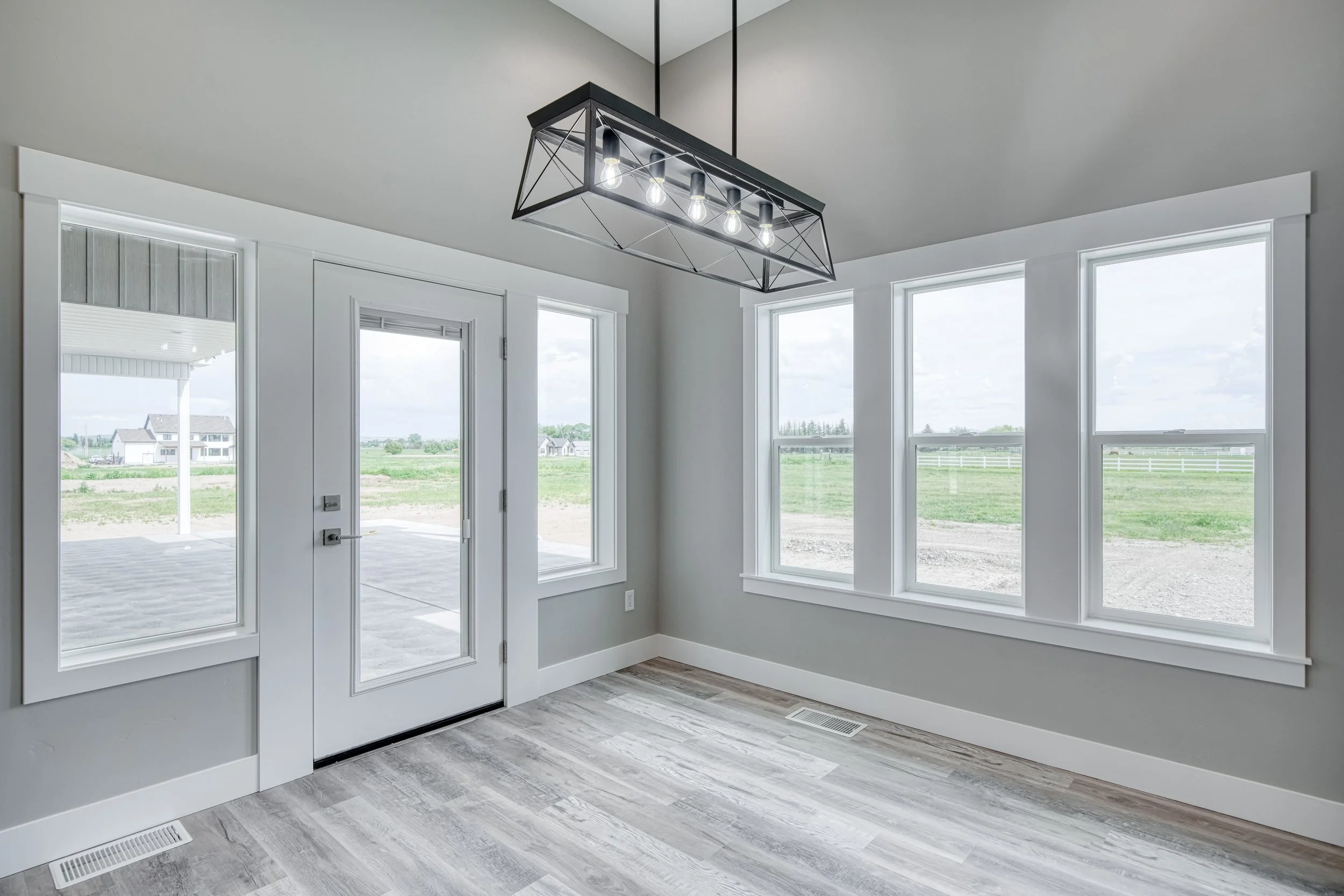 Dining area with large windows, a glass door and rectangular pendant light — JAB Construction’s Modern Craftsman custom home in Idaho Falls, Idaho.