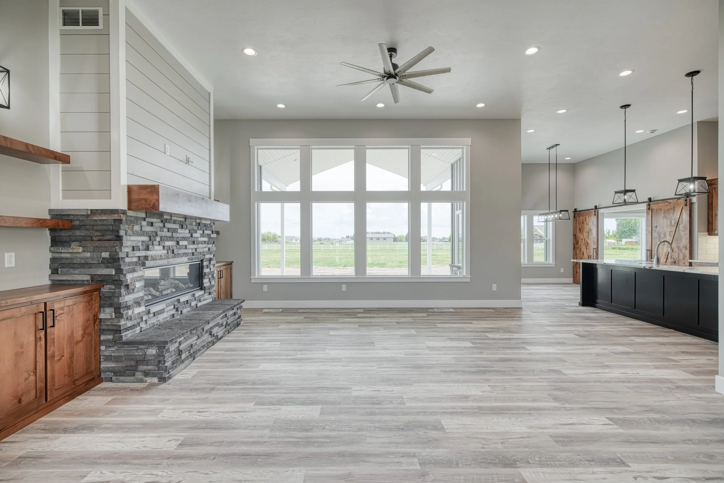 Living room with tall windows, wood-look flooring and a ceiling fan — JAB Construction’s Modern Craftsman custom home in Idaho Falls, Idaho.