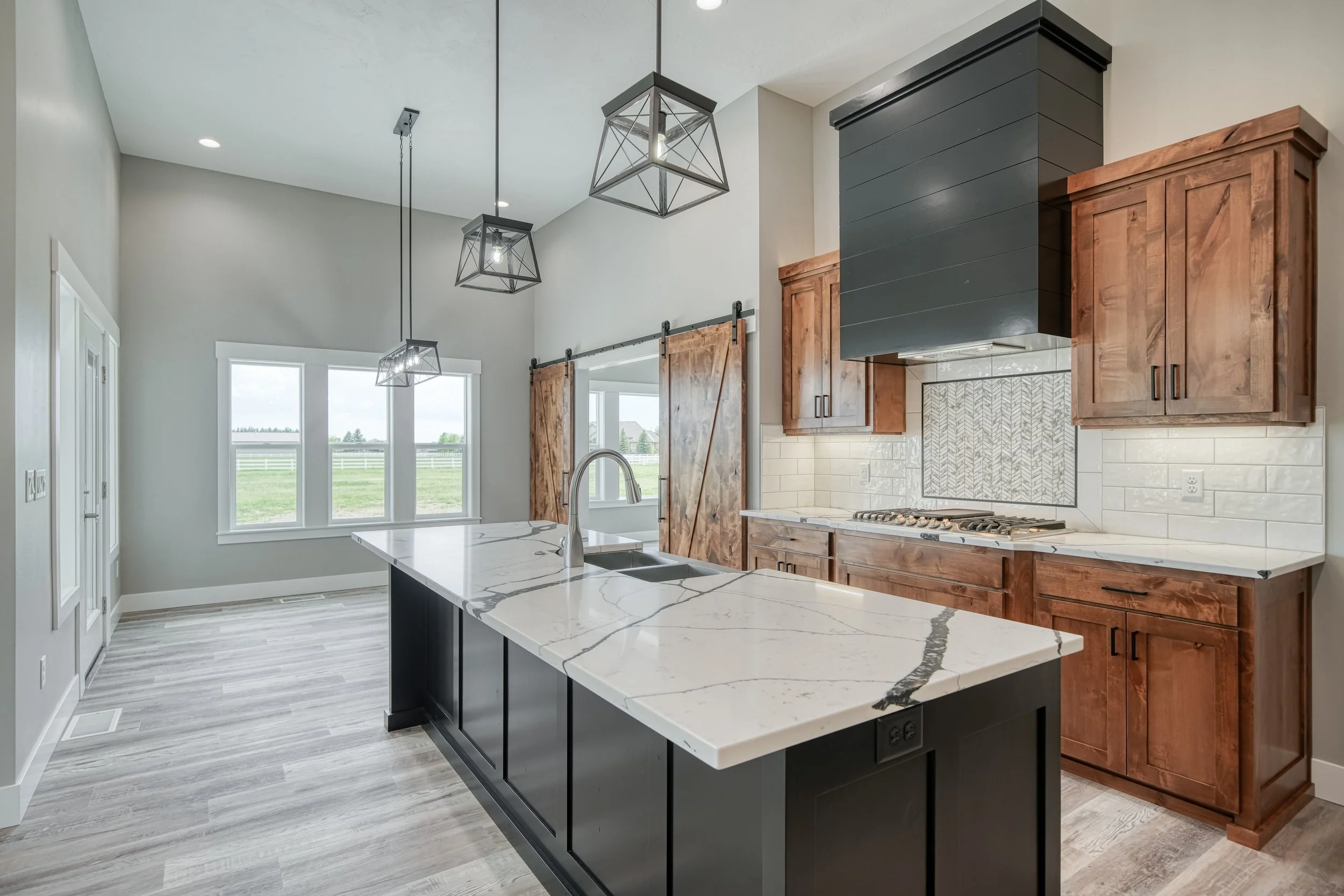 Kitchen island beside wood cabinets and a dark range hood — JAB Construction’s Modern Craftsman custom home in Idaho Falls, Idaho.