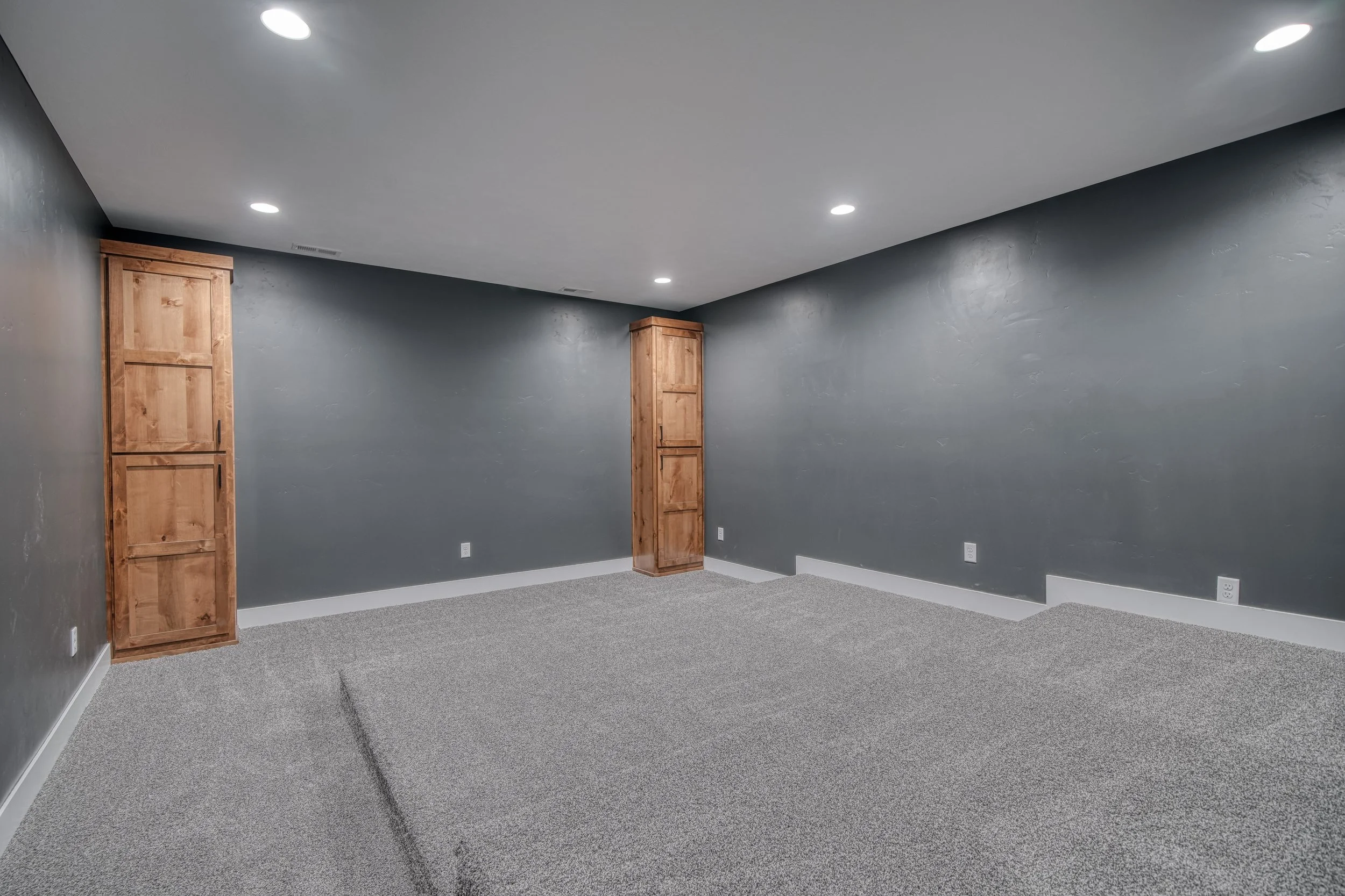 Carpeted room with dark walls and a wood door — JAB Construction’s Modern Craftsman custom home in Idaho Falls, Idaho.