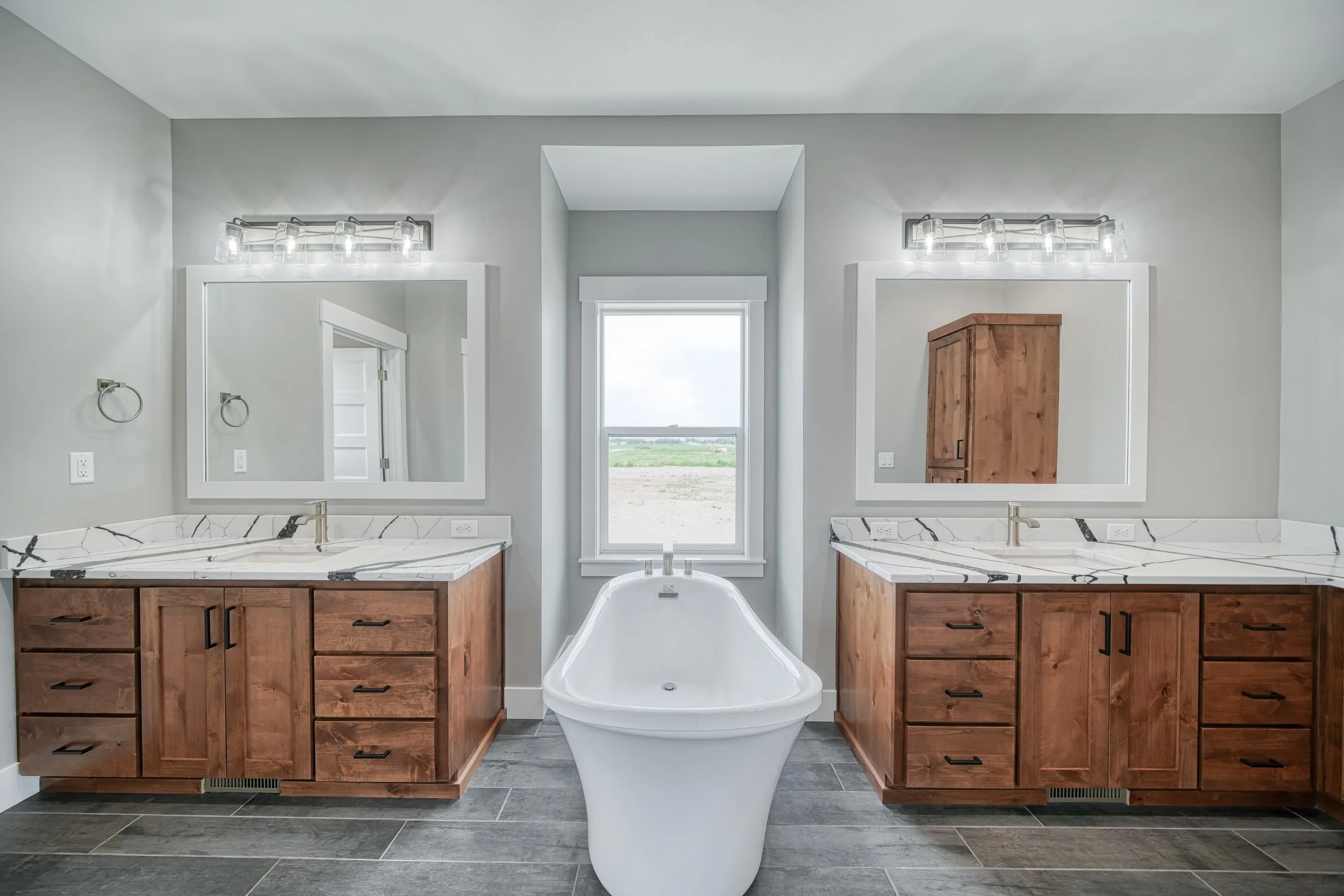 Bathroom with a freestanding tub between two wood vanities — JAB Construction’s Modern Craftsman custom home in Idaho Falls, Idaho.