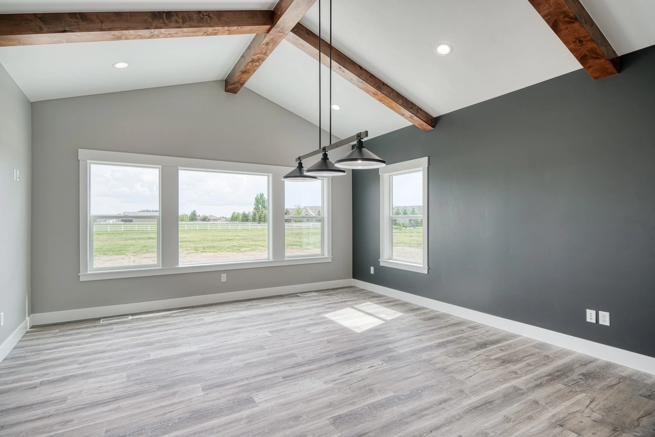 Room with exposed wood ceiling beams, large windows and a ceiling fan — JAB Construction’s Modern Craftsman custom home in Idaho Falls, Idaho.