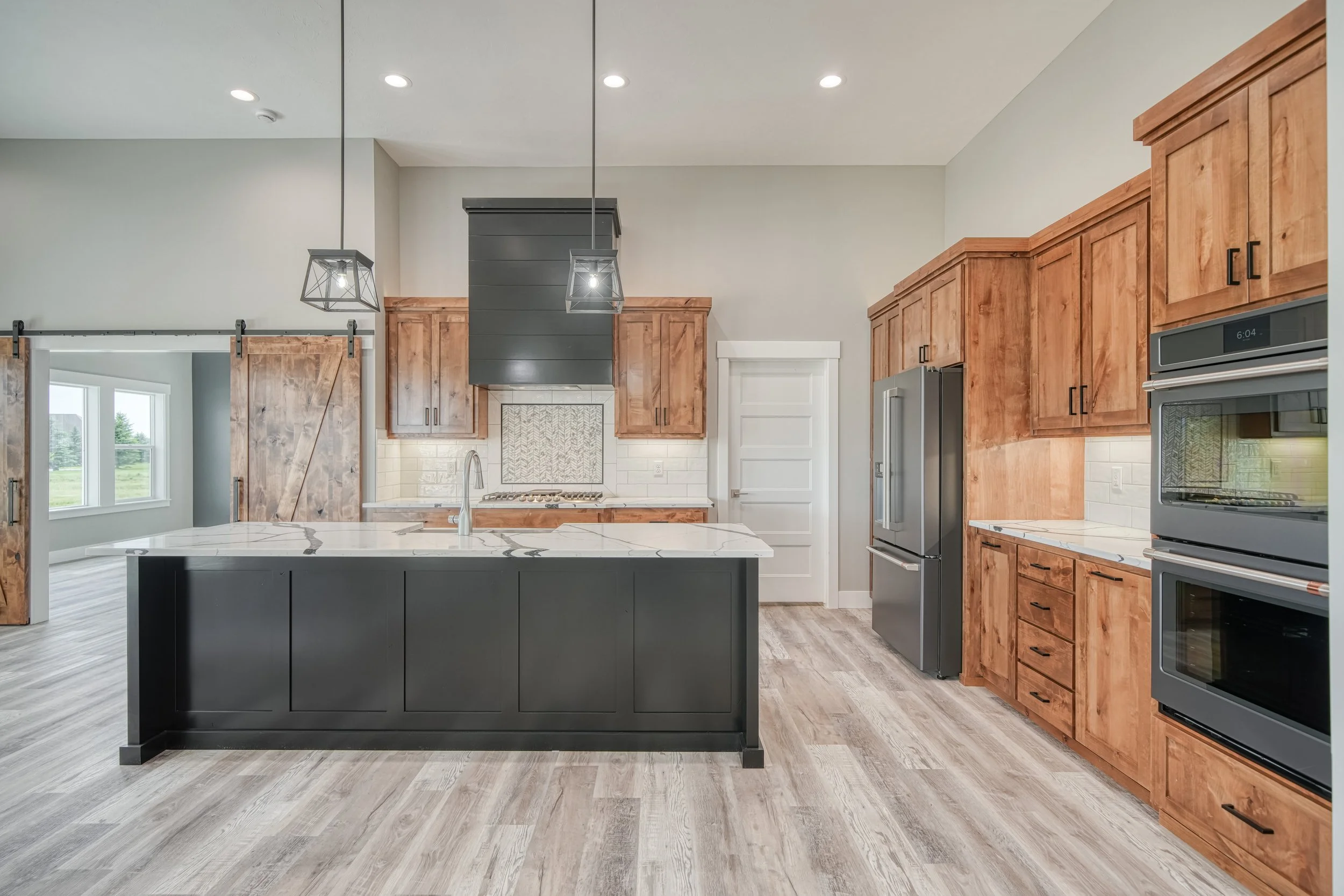 Kitchen with wood cabinets, dark island cabinetry and pendant lights — JAB Construction’s Modern Craftsman custom home in Idaho Falls, Idaho.