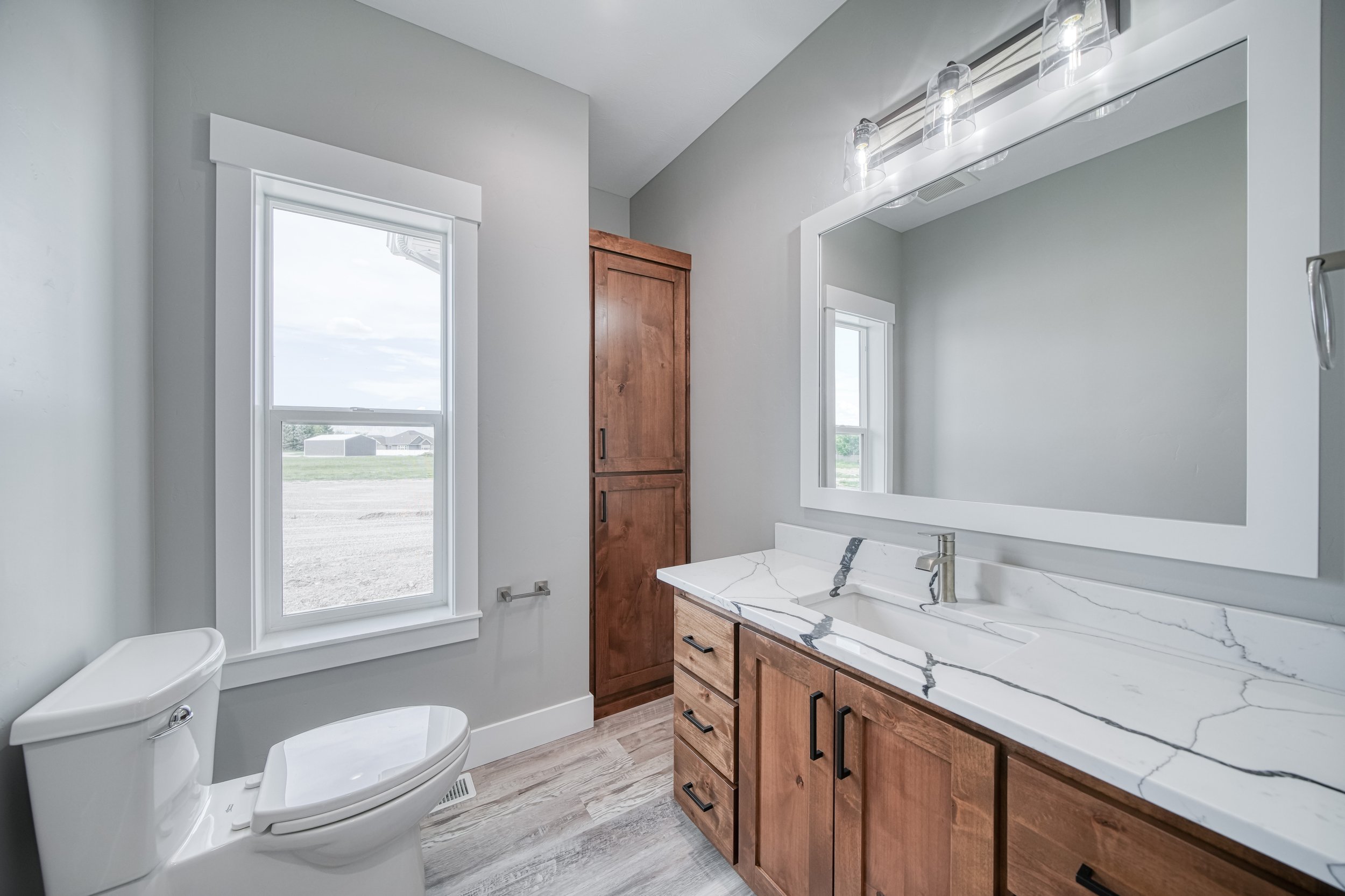 Bathroom with a tub, wood vanity and large window — JAB Construction’s Modern Craftsman custom home in Idaho Falls, Idaho.