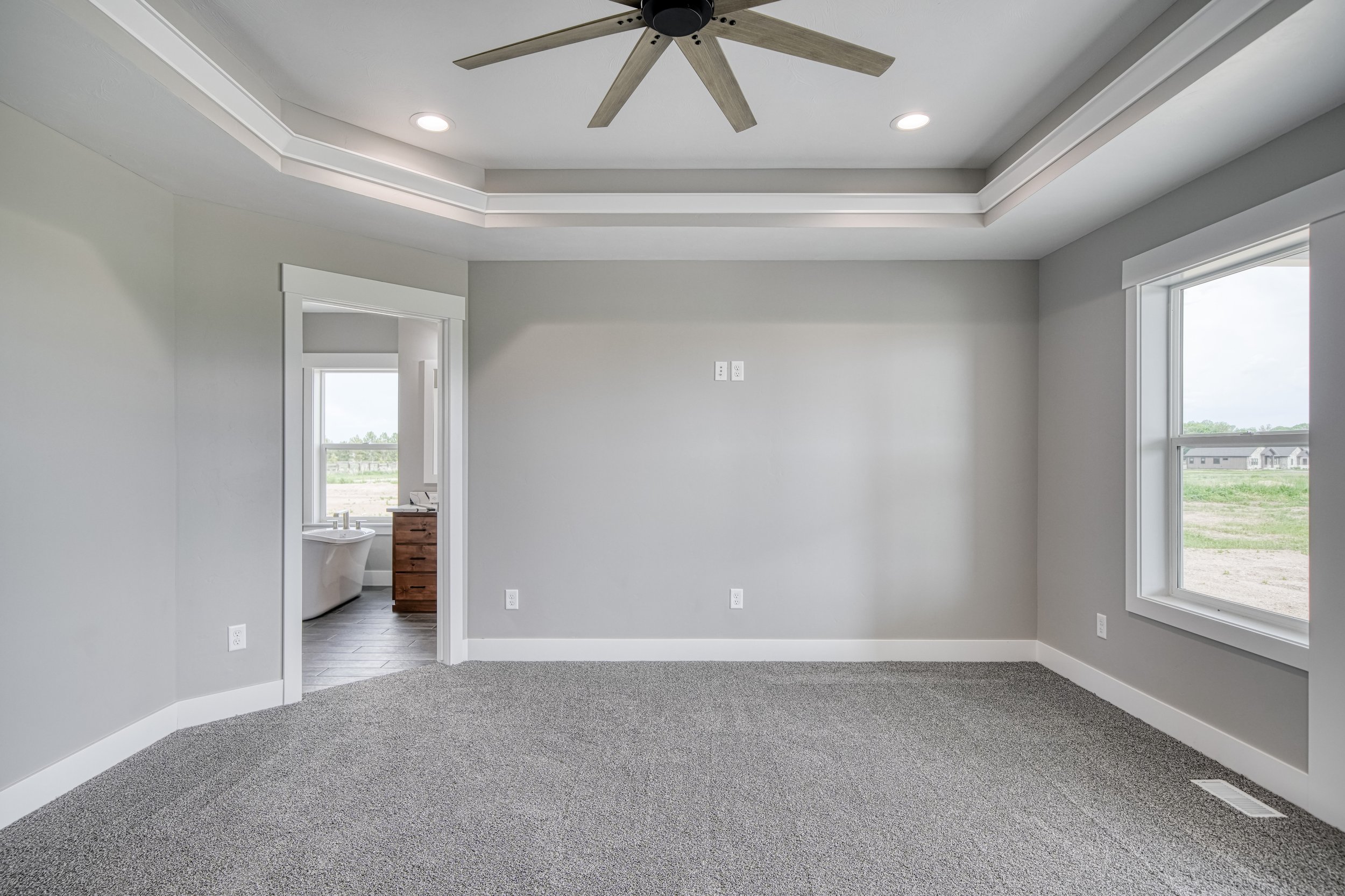 Carpeted bedroom with a tray ceiling and ceiling fan — JAB Construction’s Modern Craftsman custom home in Idaho Falls, Idaho.
