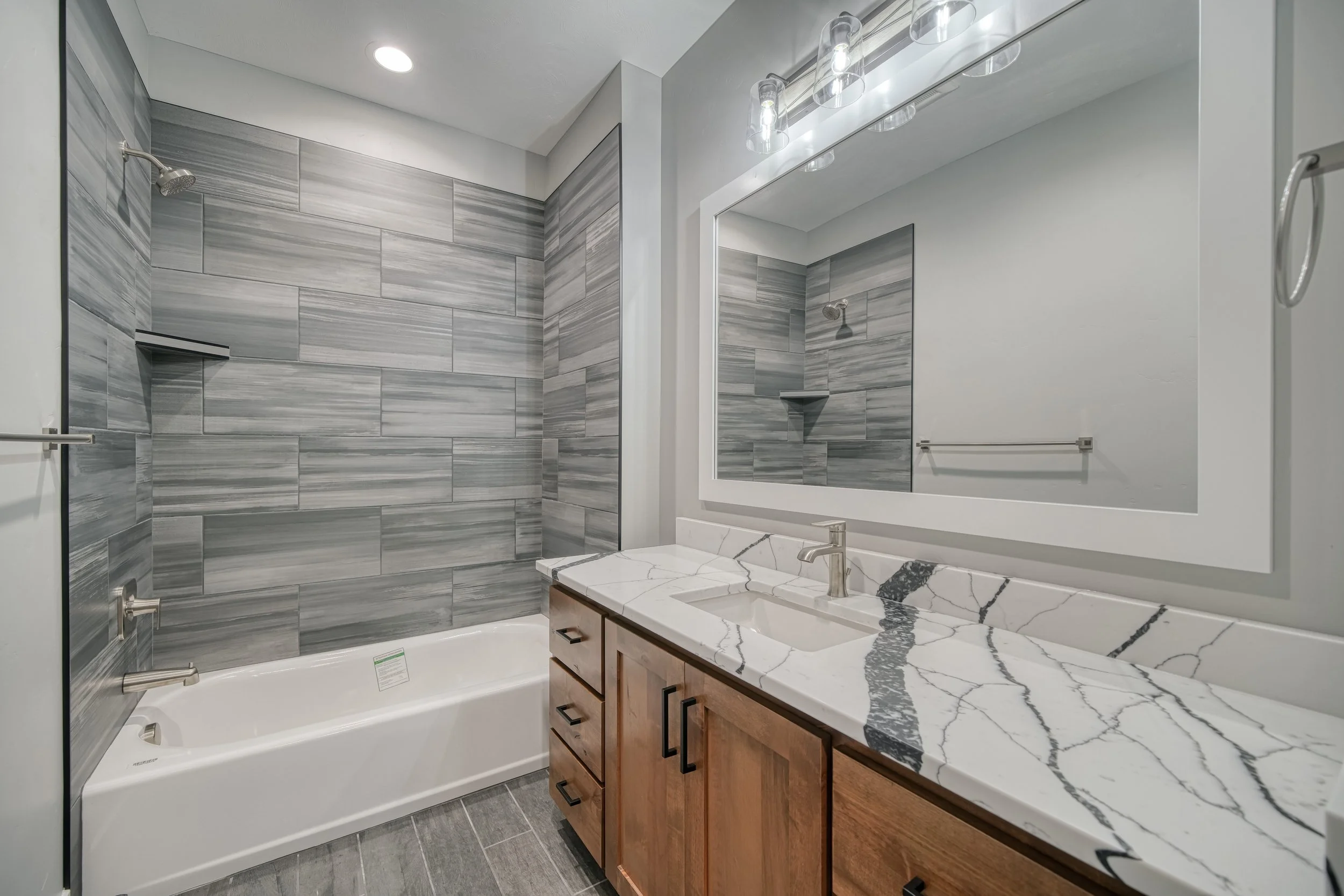 Wood bathroom vanity with a light countertop and large mirror — JAB Construction’s Modern Craftsman custom home in Idaho Falls, Idaho.