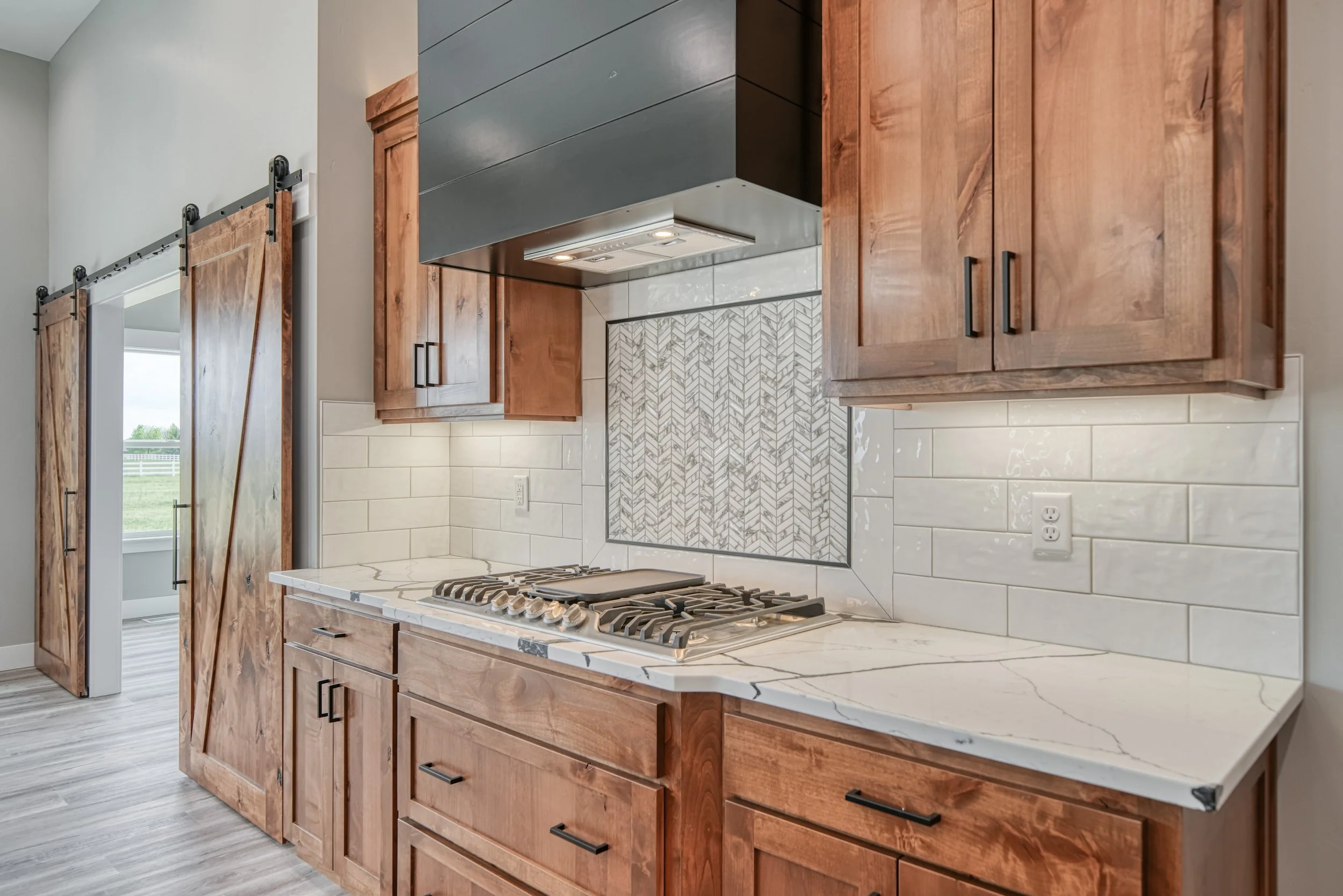 Dark kitchen range hood with wood cabinetry and patterned backsplash — JAB Construction’s Modern Craftsman custom home in Idaho Falls, Idaho.