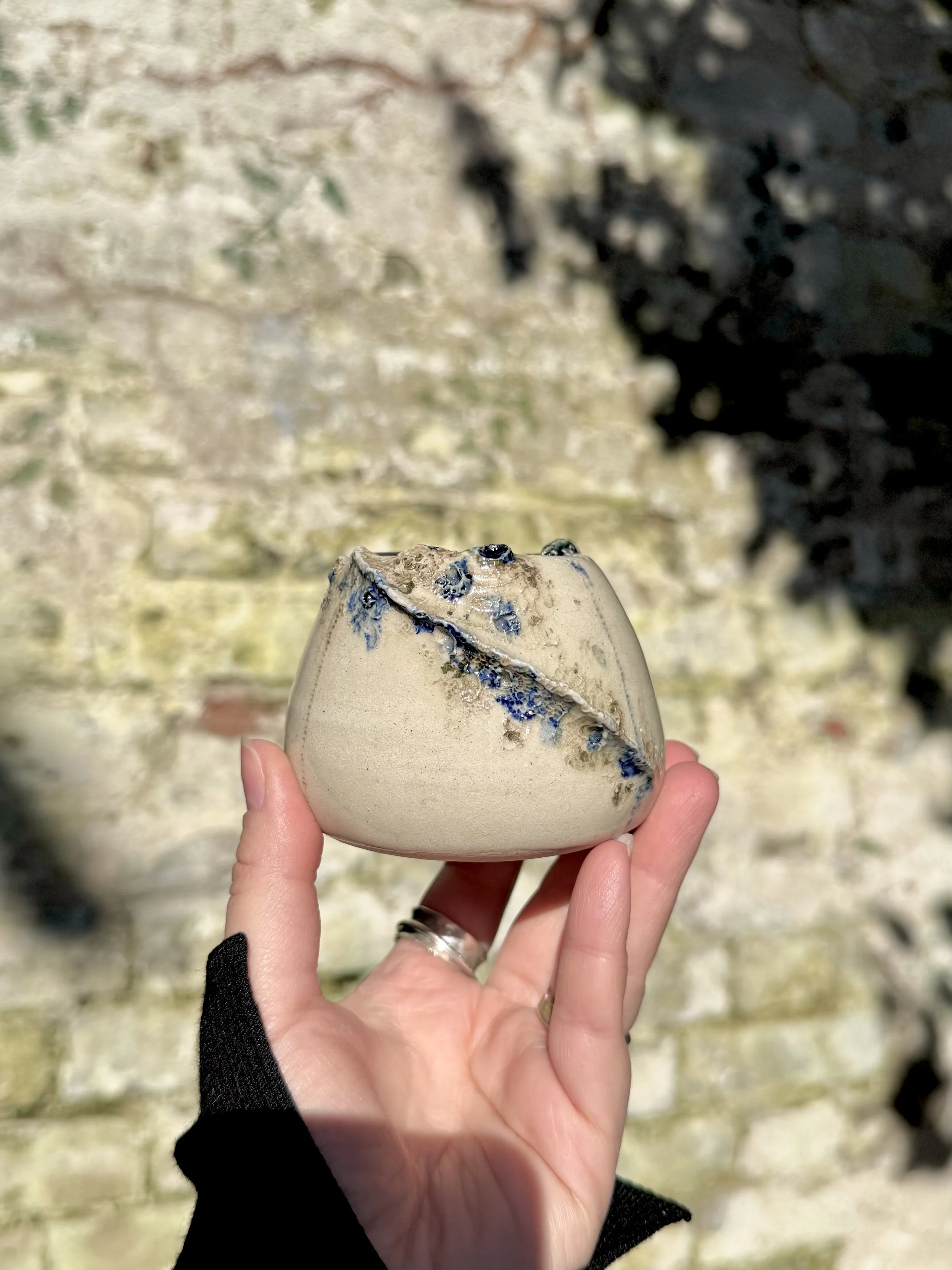 A small ceramic vase with blue accents, textures from the sea. Photographed in nature.