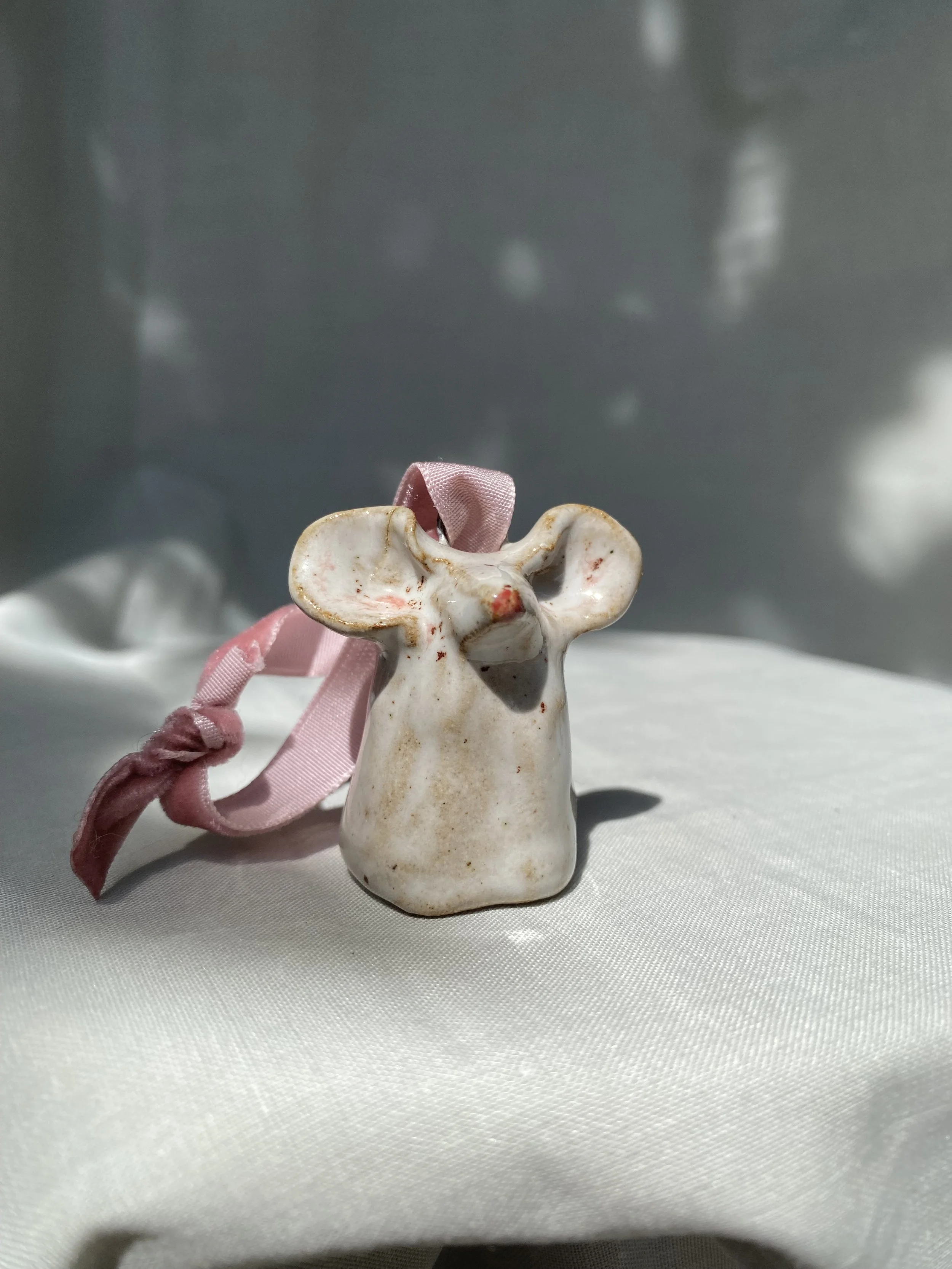 A ceramic figurine of a dog with a pink ribbon tied around its neck, placed on a white surface with a blurred gray background.