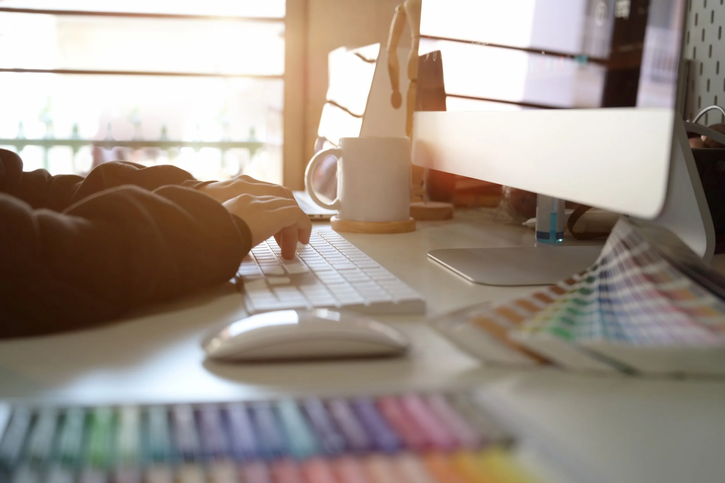 Creative workspace with a design monitor, keyboard, and color swatches in warm natural light