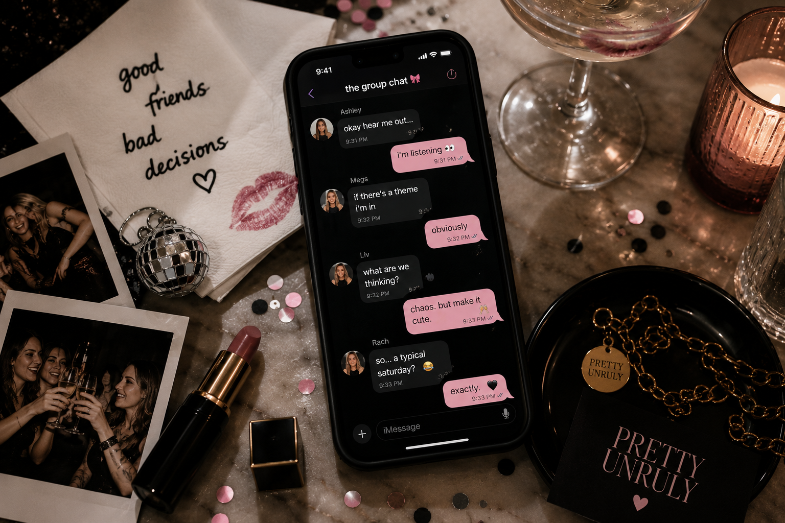 A smartphone displaying a group chat on a party or celebration table surrounded by photographs, jewelry, confetti, lipstick, candles, and pink themed decorations.