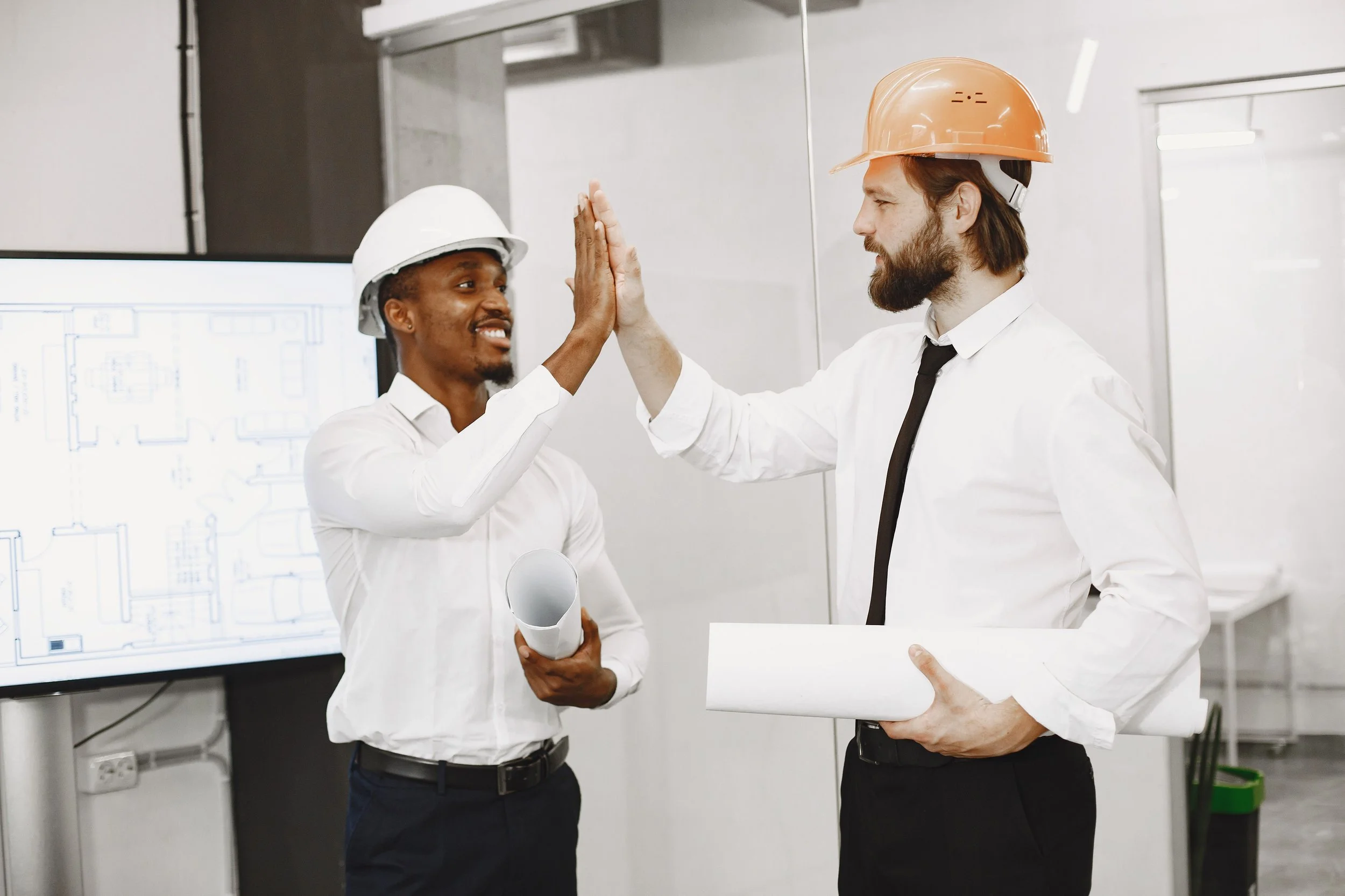 Two project team members in hard hats sharing a high five in front of building plans