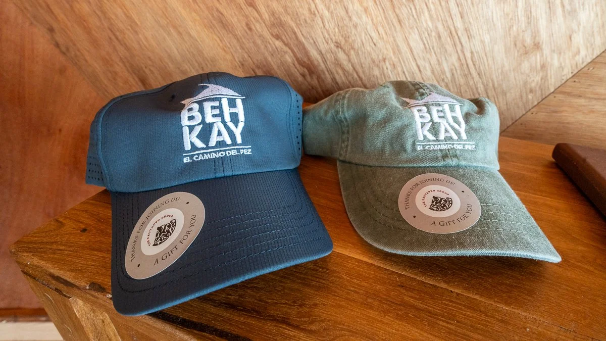 Two BEH Kay baseball caps, one in blue and one in green, on a wooden surface.