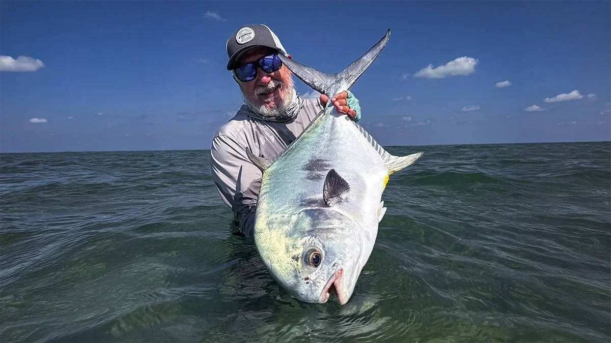 A man wearing sunglasses and a cap holding a large fish in the ocean.