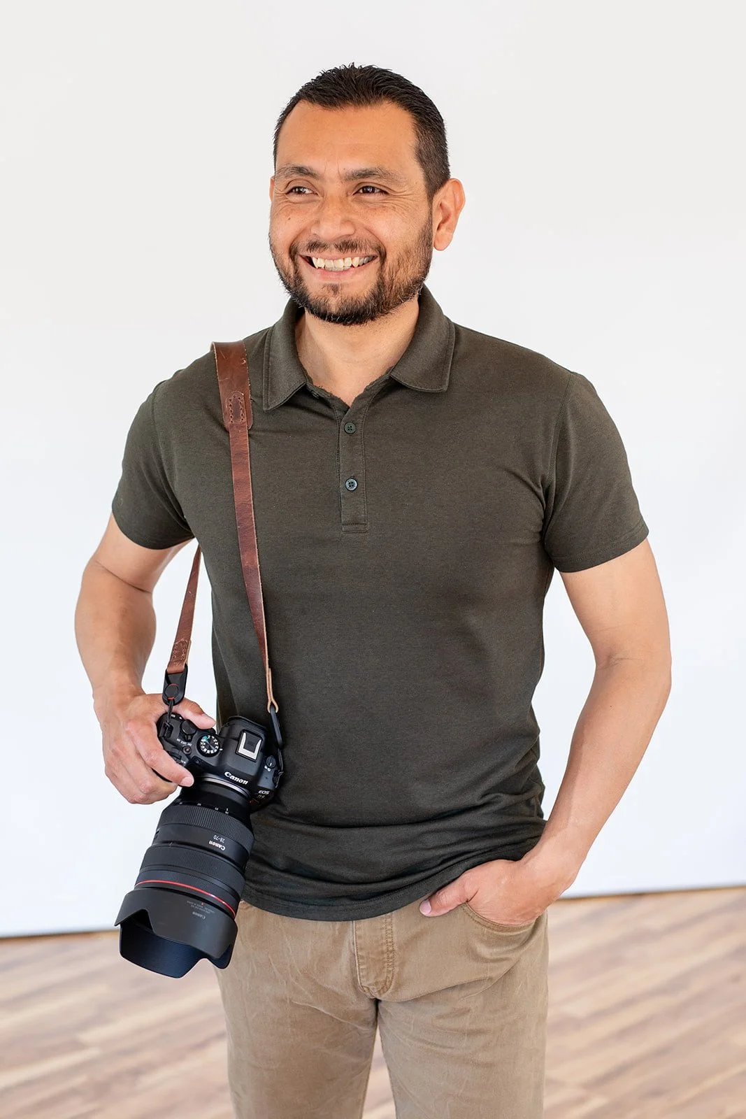 A smiling man with a camera around his neck standing against a white background.