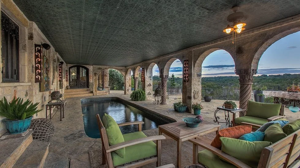 Covered pool patio with stone columns, green cushioned chairs, and scenic hill views at a luxury home in Austin