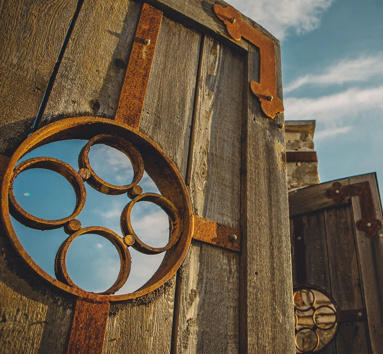 Close-up of rusty metal decorative circular frame attached to wooden fence panels under a partly cloudy sky.