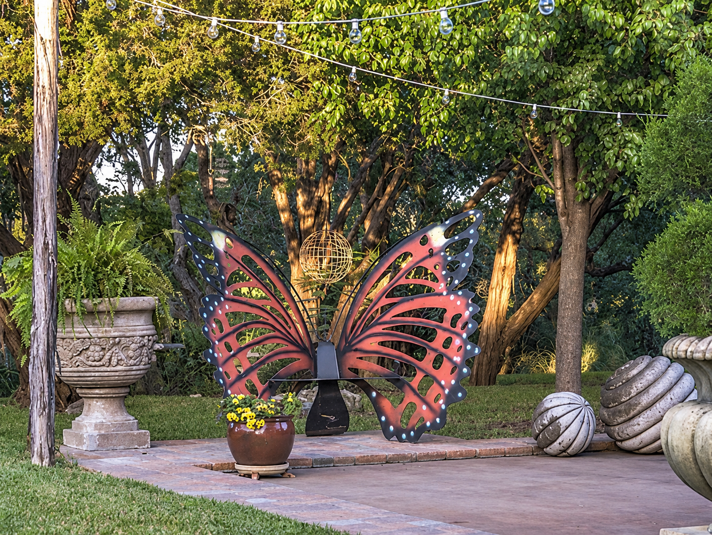 Large red and black butterfly sculpture in a garden surrounded by trees and stone planters in Austin
