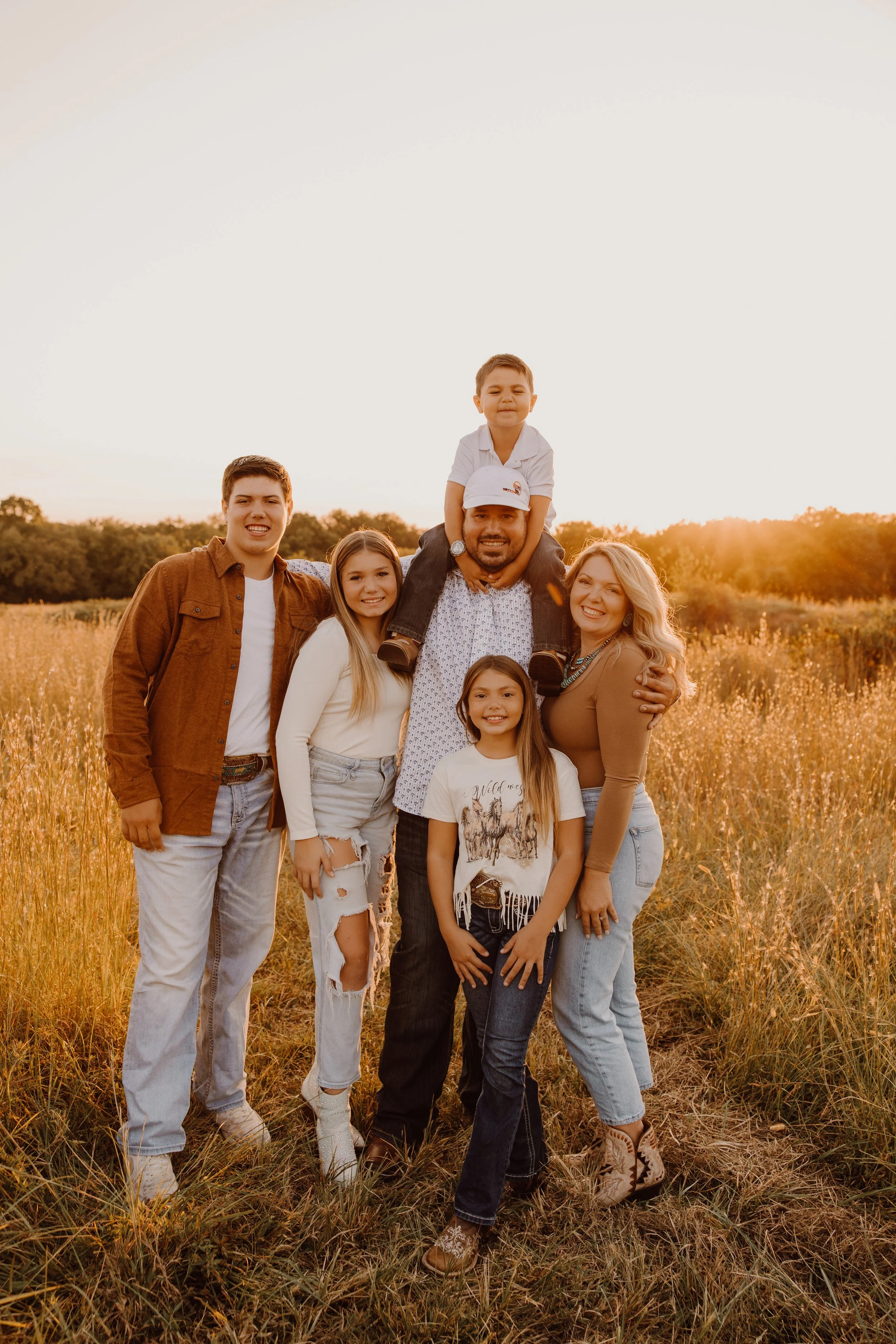 A family of seven standing in a field at sunset, smiling and posing for a photo.