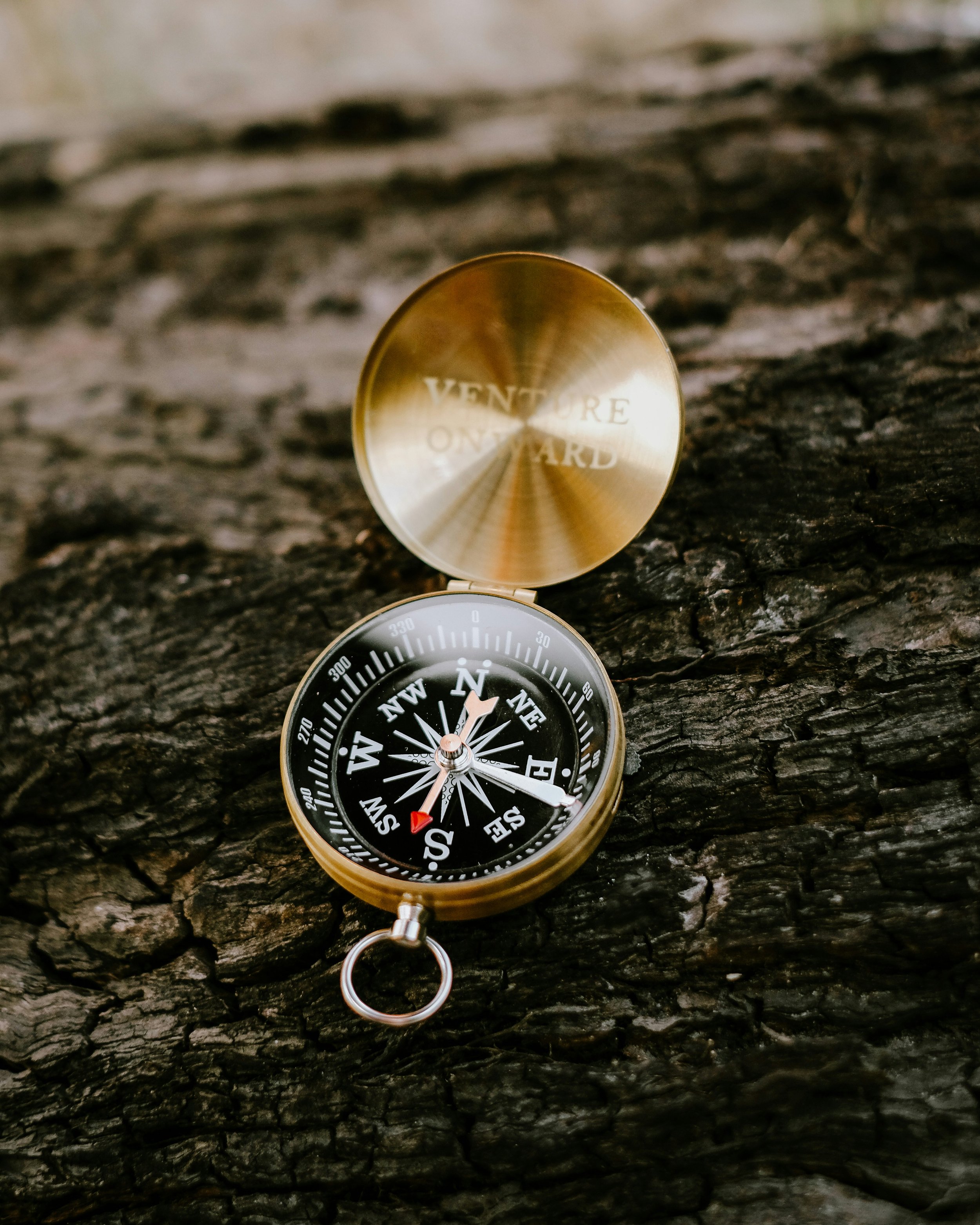 A compass and a golden badge with the words 'Venture Beyond' on it, resting on a rough, dark wooden surface.