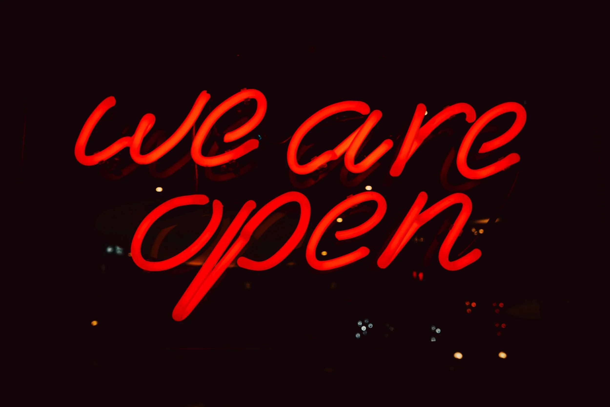 Red neon sign reading 'CUE CARE OPEN' against a dark background.
