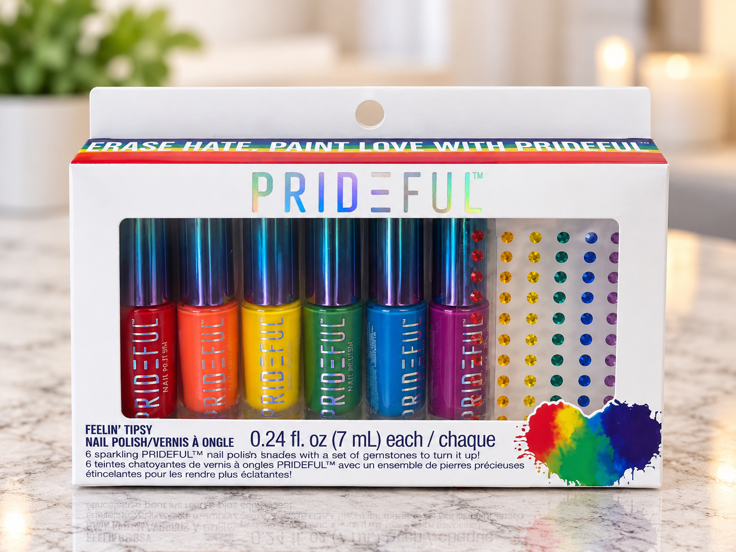 Set of six rainbow-colored PrideFUL nail polishes in rainbow packaging with a rainbow, gem-like accents inside a white box with rainbow across the top and rainbow dots on the side, on a marble surface with blurred background.
