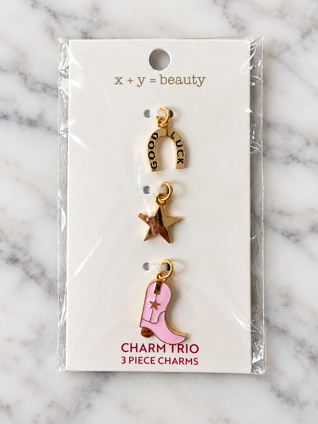 Pack of three charm trios with gold-tone metal charms, including a horseshoe with 'GOOD LUCK' inscribed, a pink cowboy boot with a star, and a gold star, on a white card with the phrase 'x + y = beauty' at the top.