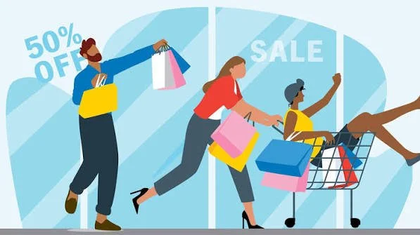 People shopping during a sale, with a large sign saying 50% off and another labeled SALE, carrying shopping bags and pushing a shopping cart.