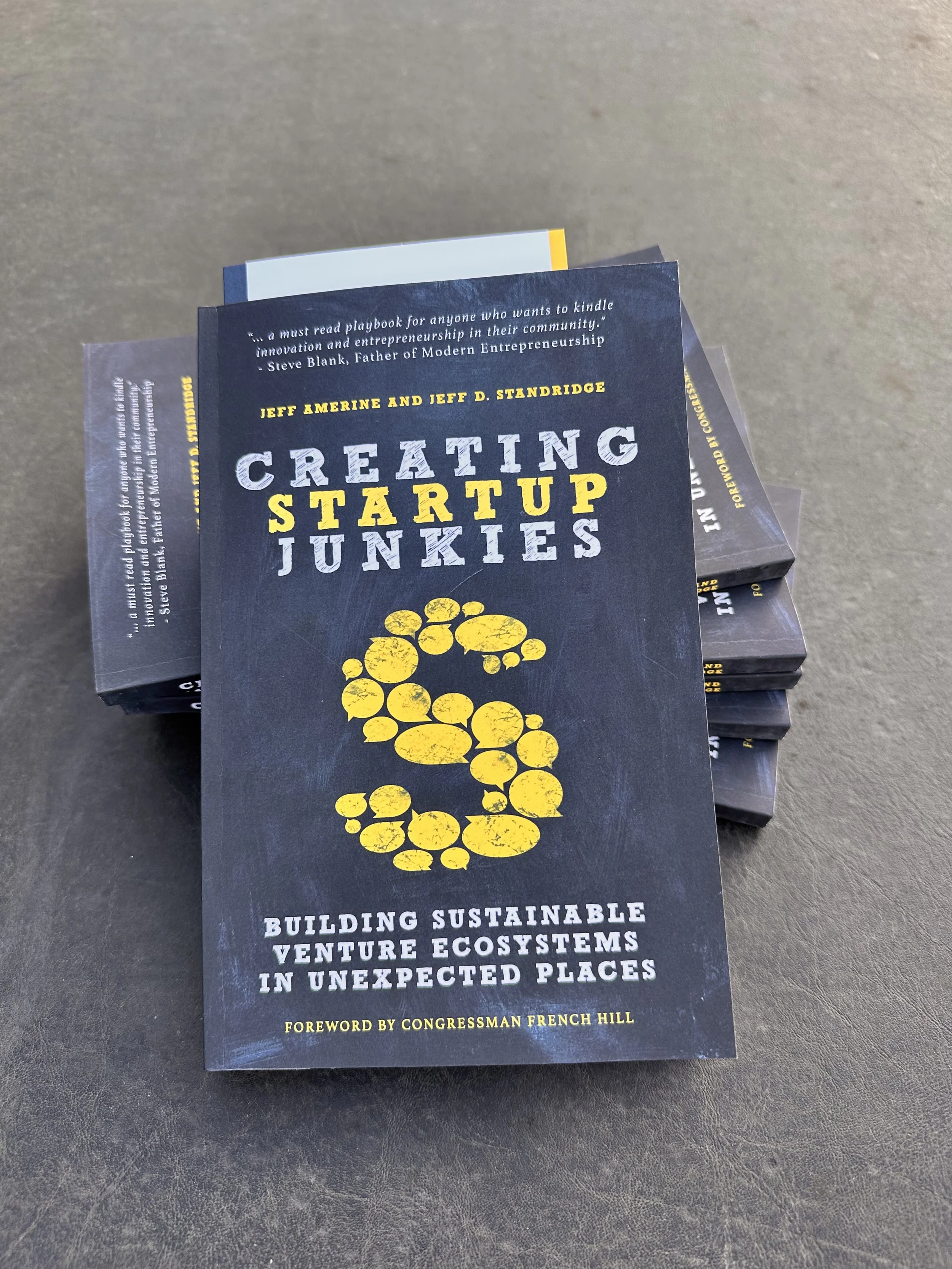 Stack of books with the front book titled "Creating Startup Junkies" by Jeff Amerine and Jeff D. Standridge on a dark surface.