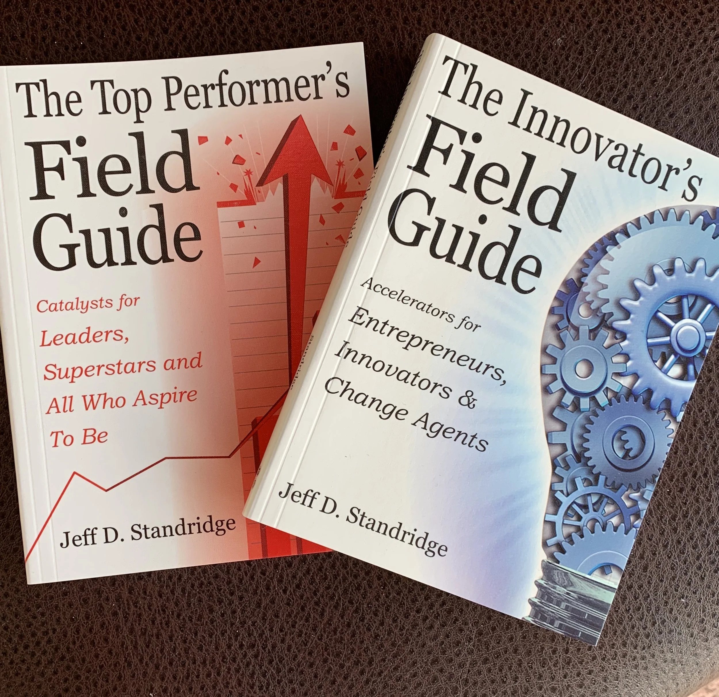 Close-up of two books titled 'The Top Performer's Field Guide' and 'The Innovator's Field Guide' placed on a dark brown textured surface.