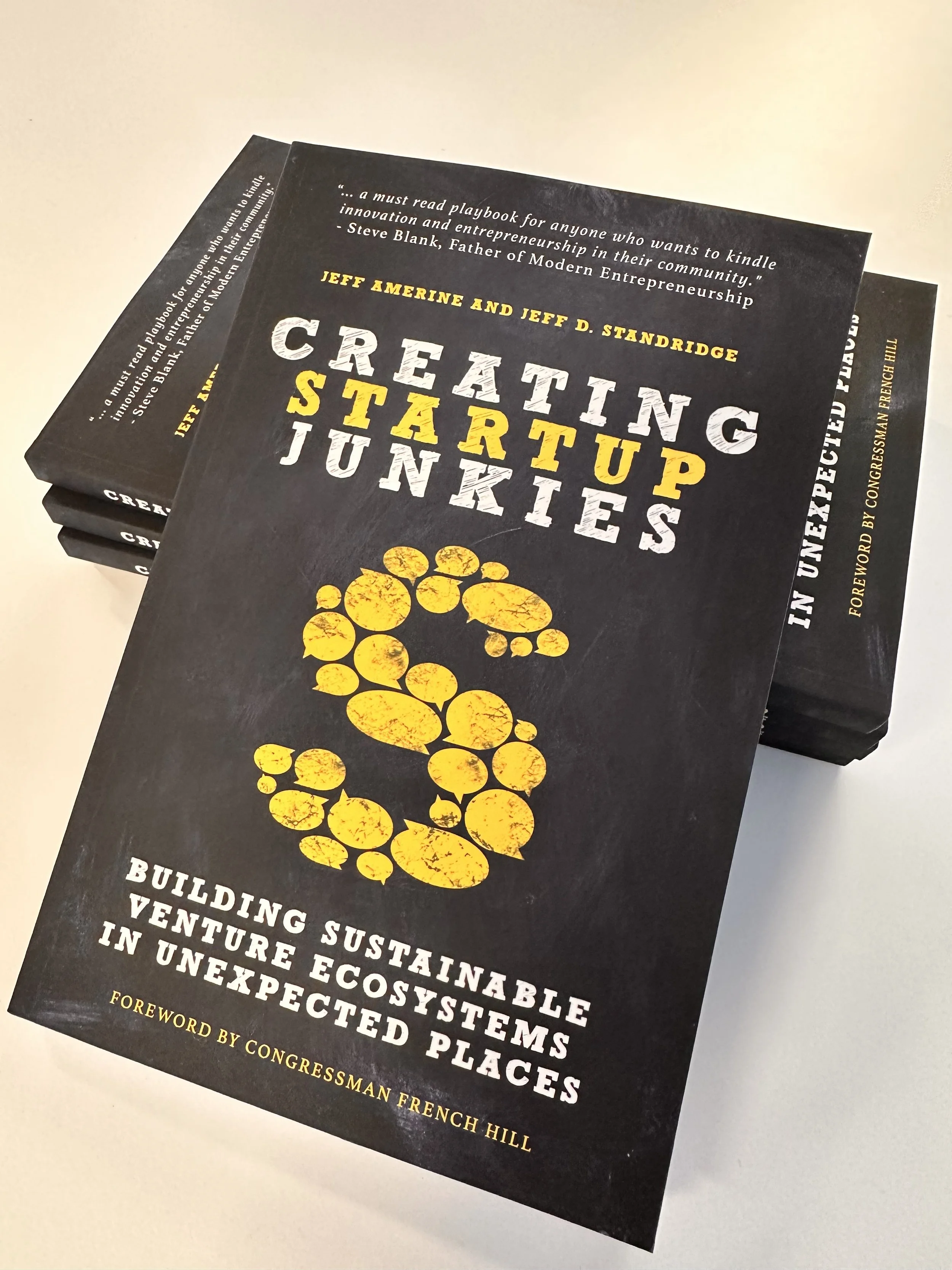 Book titled "Creating Startup.j" with a yellow paw print on the cover, stacked among other copies on a white surface.