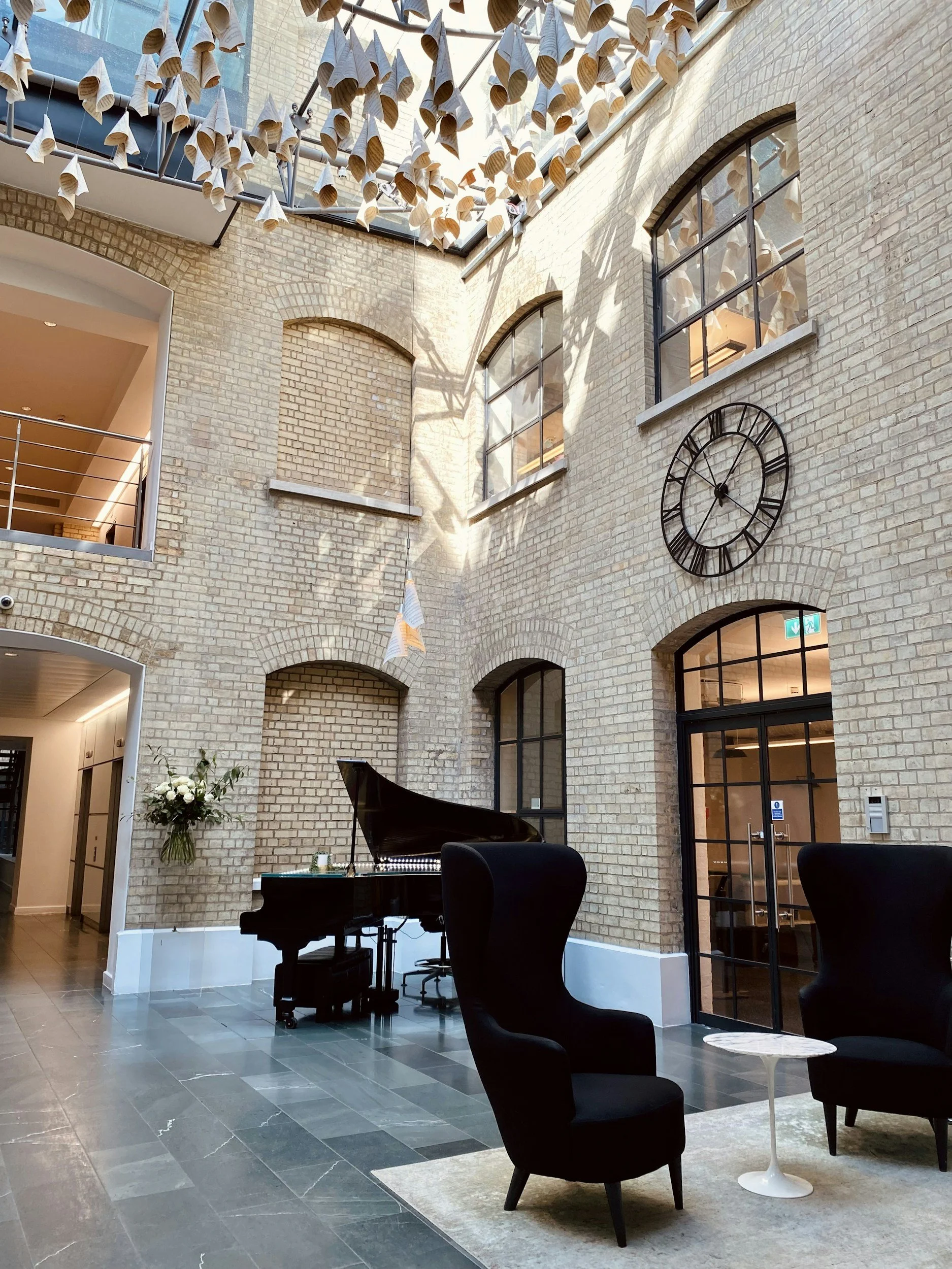 the atrium lobby of a brick building with highback black chairs and a grand piano
