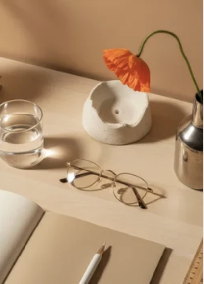 a desk with a notebook, a pen, a glass of water, eyeglasses, and an orange flower in a small vase