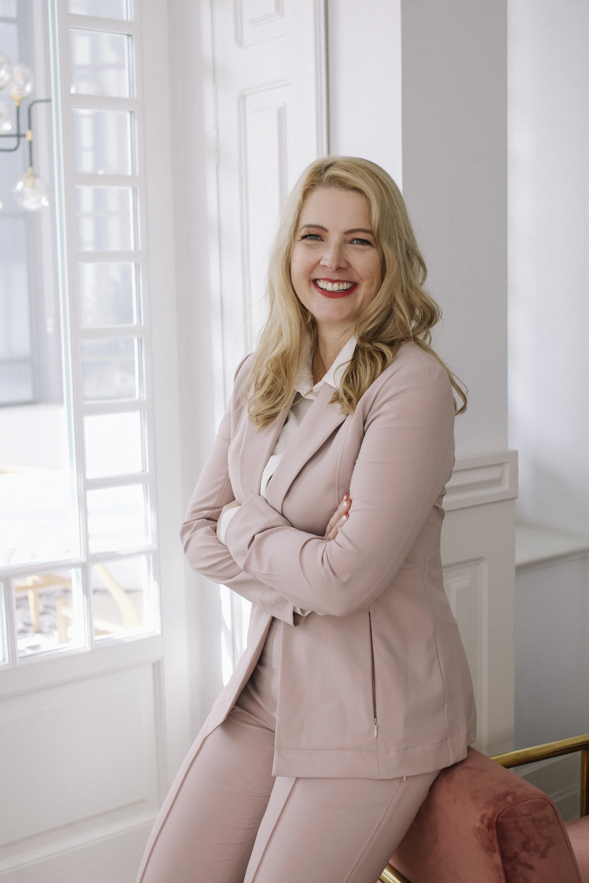 photo of Amy Short with her arms crossed. She is leaning on a chair and wearing a pink suit.