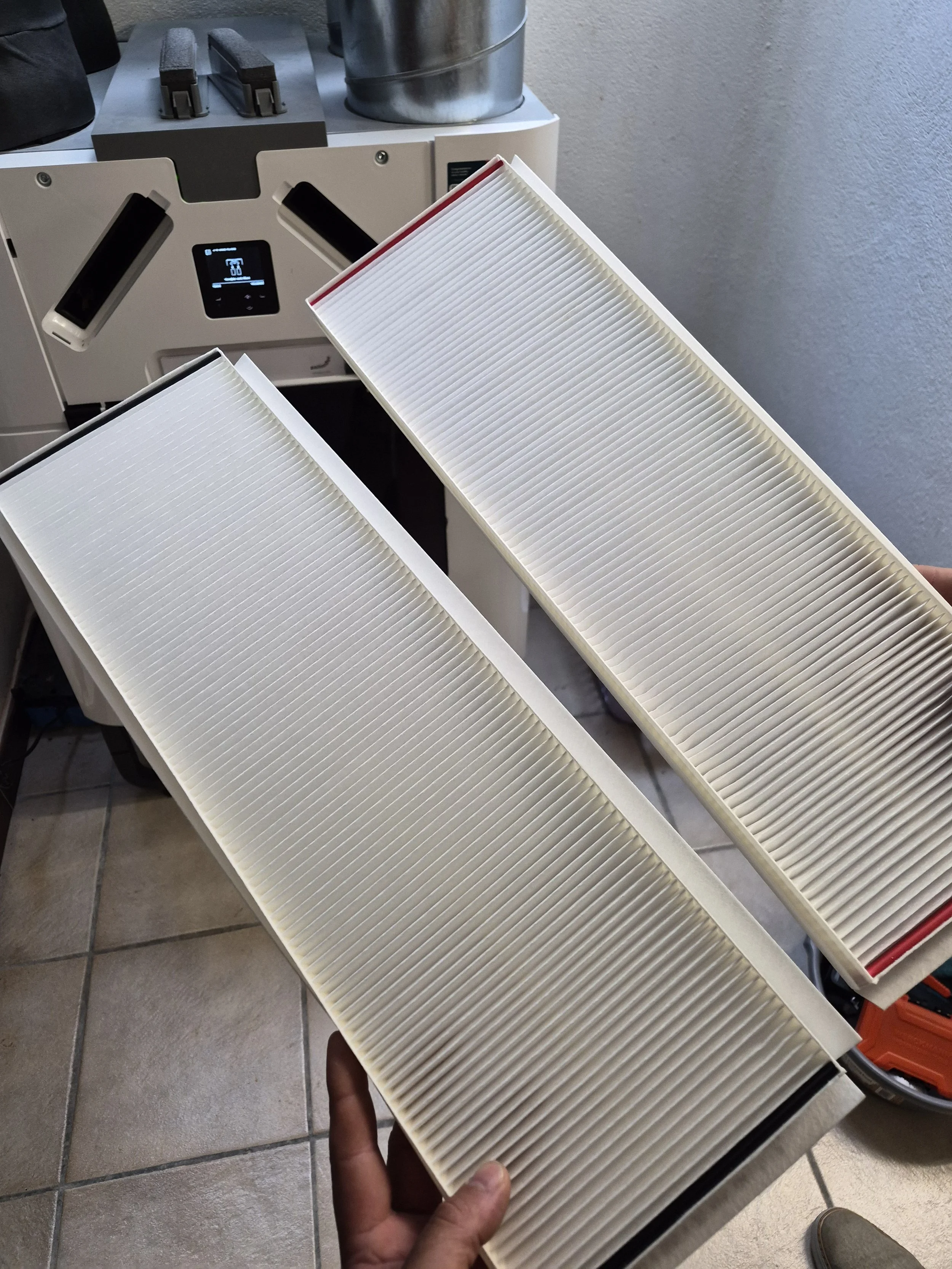 Person holding a new clean air filter in front of a cabinet with additional filters and cleaning tools.
