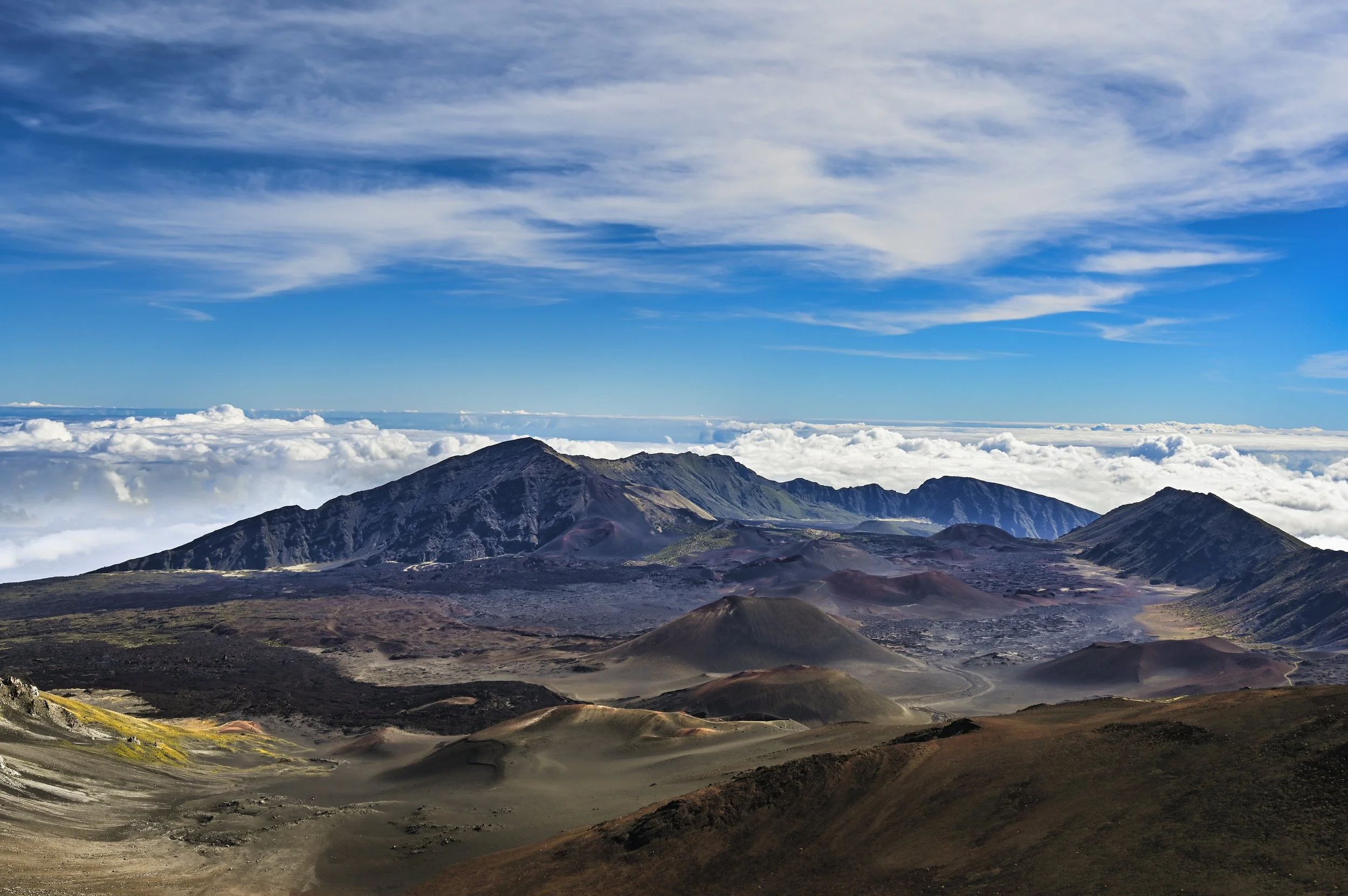 A mountainous landscape with volcanic terrain, dark volcanic hills, and a sky filled with clouds.