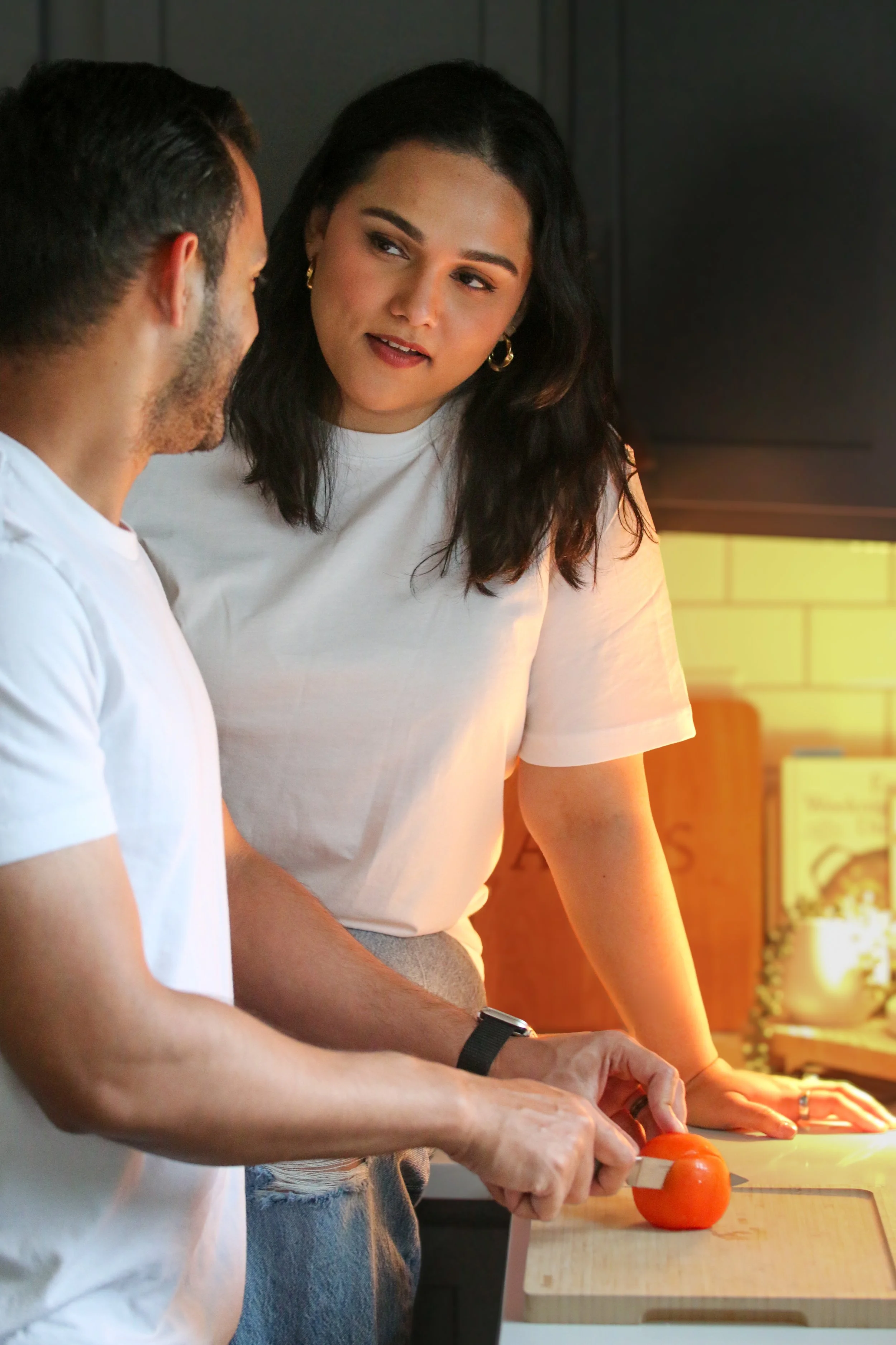Two people slicing tomatoes on a cutting board in a kitchen.