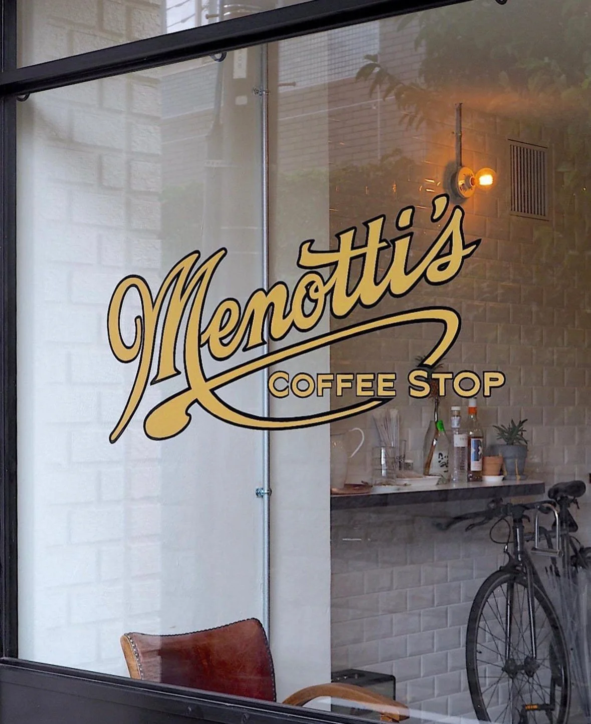 The gold Menotti's Coffee Stop sign on a white tiled wall in Tokyo