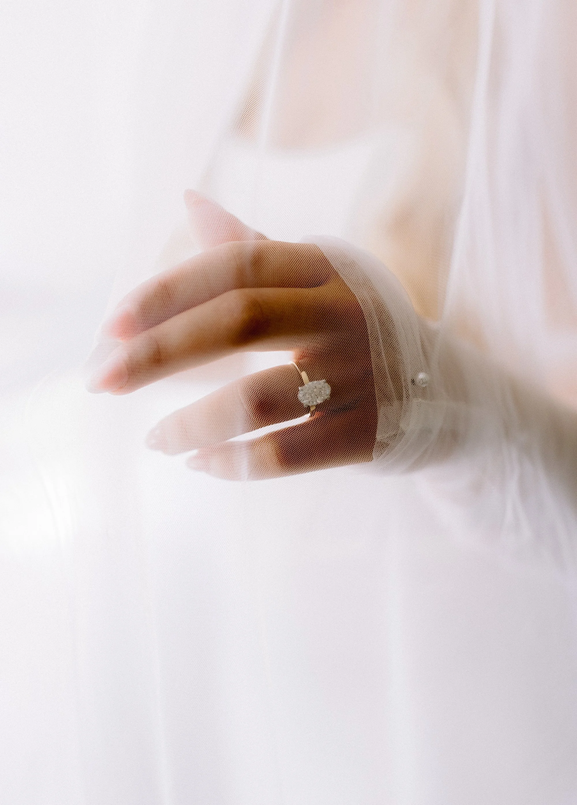 Close-up of a hand with a diamond ring, pressing against a semi-transparent white fabric or curtain.