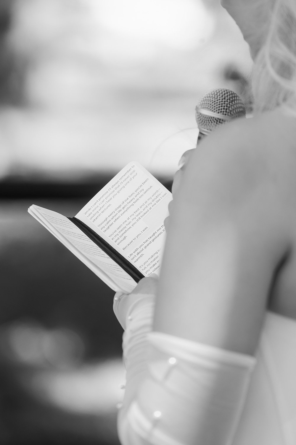 Person reading a book and speaking into a microphone in black and white.
