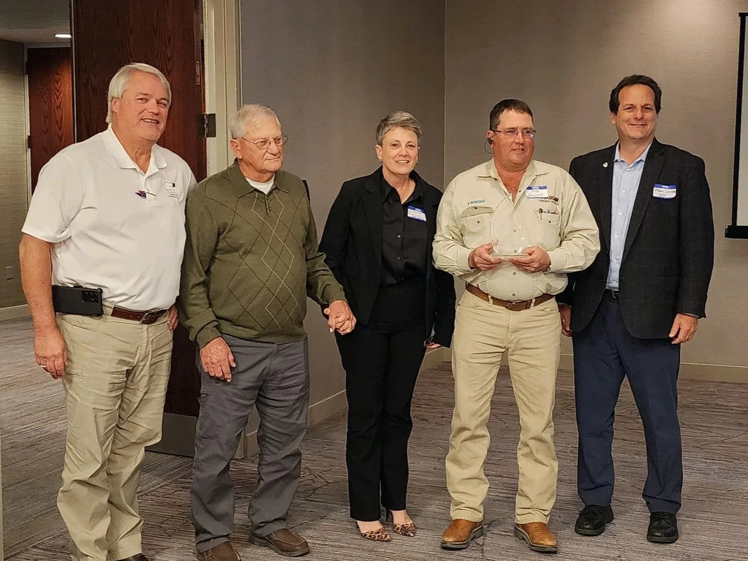 Group of five people standing together during an award ceremony or event indoors, with one person holding a clear award trophy.