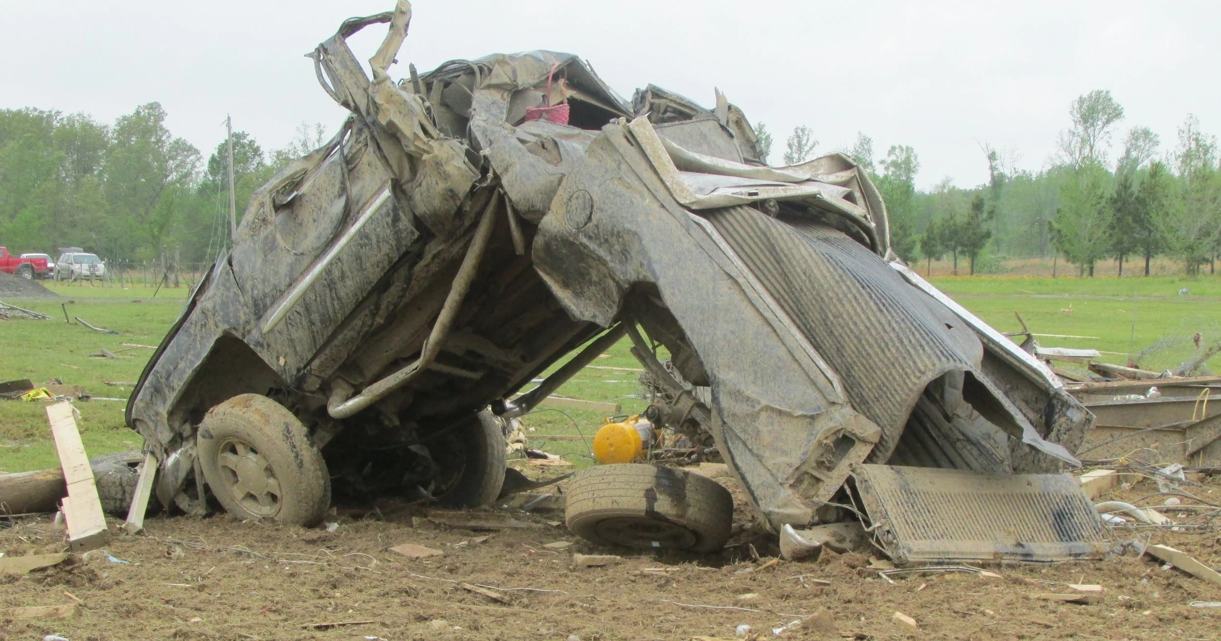 Damaged vehicle wreckage after a crash in a field with trees in the background.