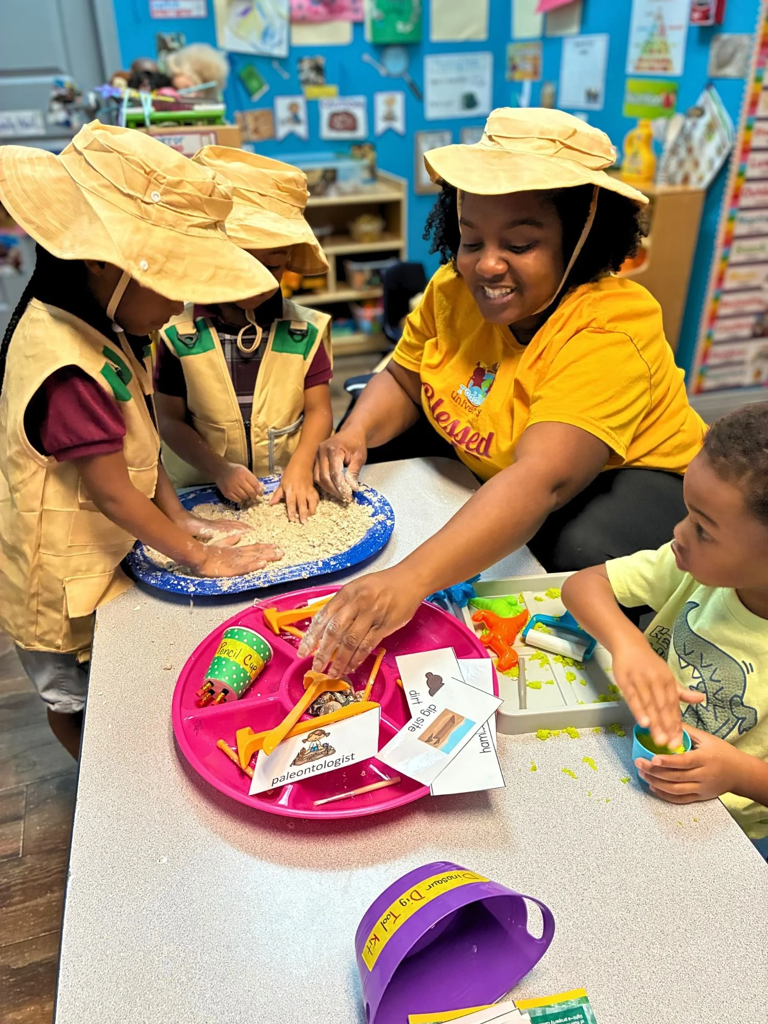 Students and teacher participate in a hands-on paleontology activity, searching through sand for and identifying artifacts at Toddler’s University.