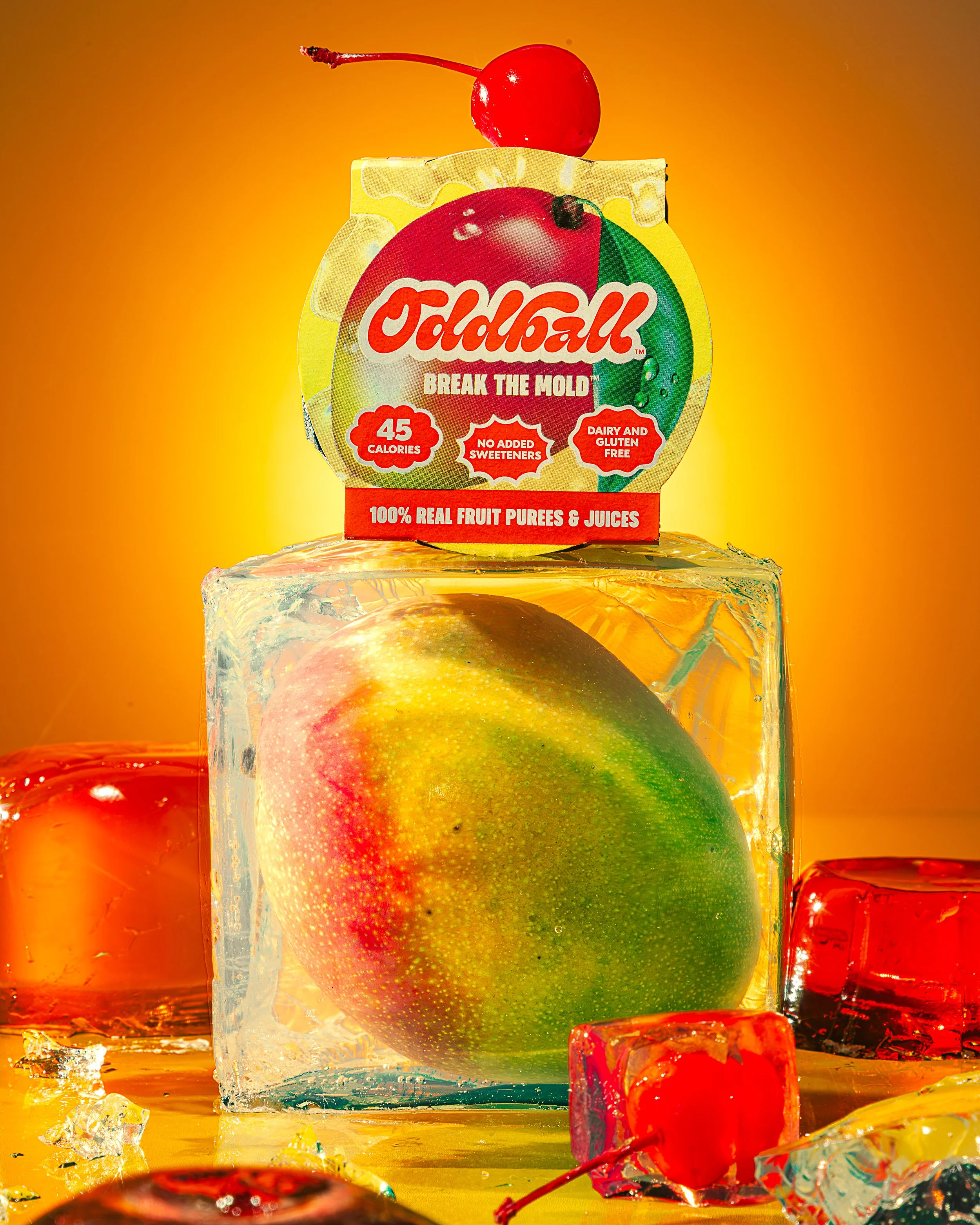 Close-up of a cherry on top of a fruit puree package labeled 'Old Bay' with the tagline 'Break the Mold,' featuring a red, green, white, and yellow color scheme. The background is a gradient of orange and yellow. There are ice cubes, cherries, and fr