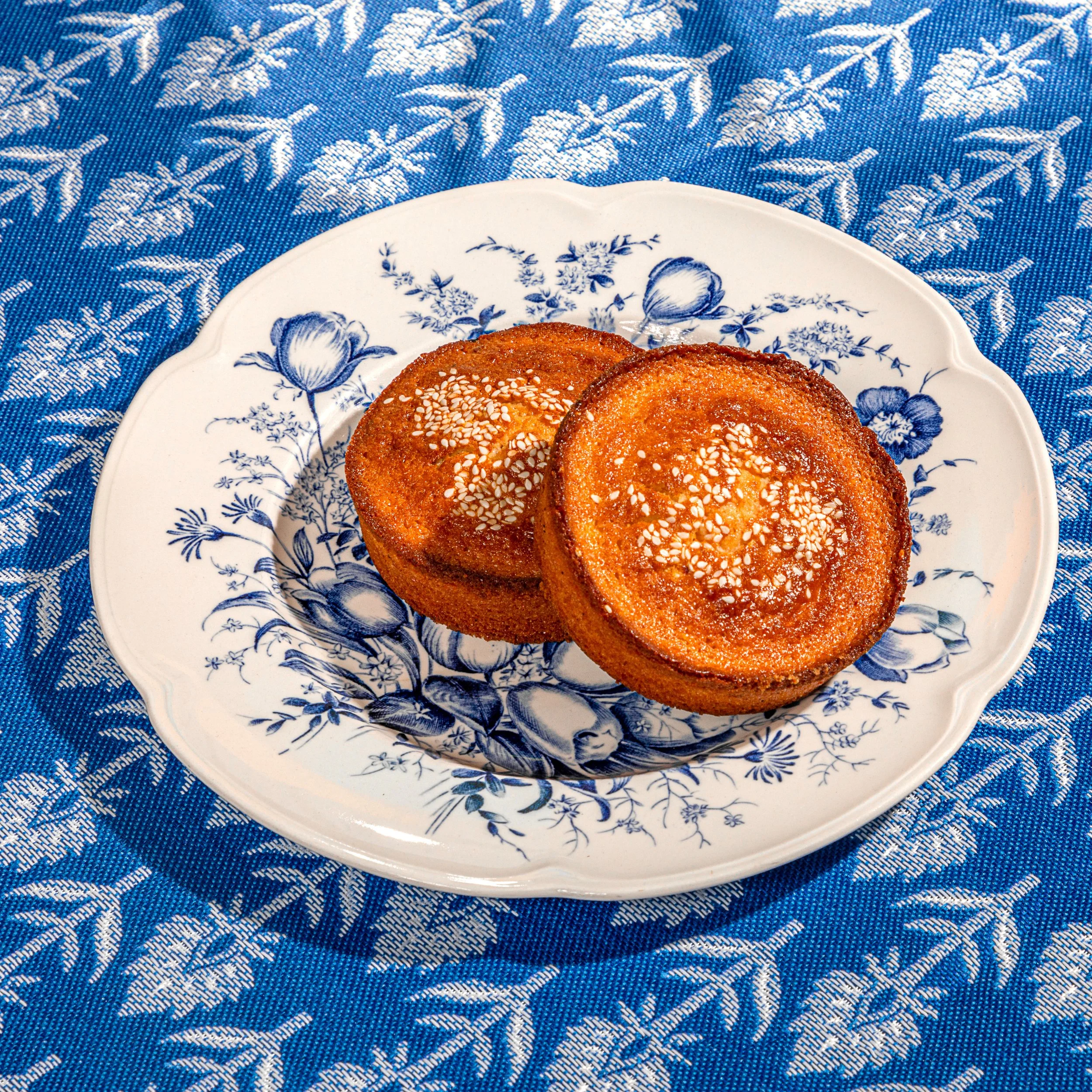 Close-up of a white and blue floral patterned plate with a textured edge, placed on a blue and white textile background, with some food items on the plate.