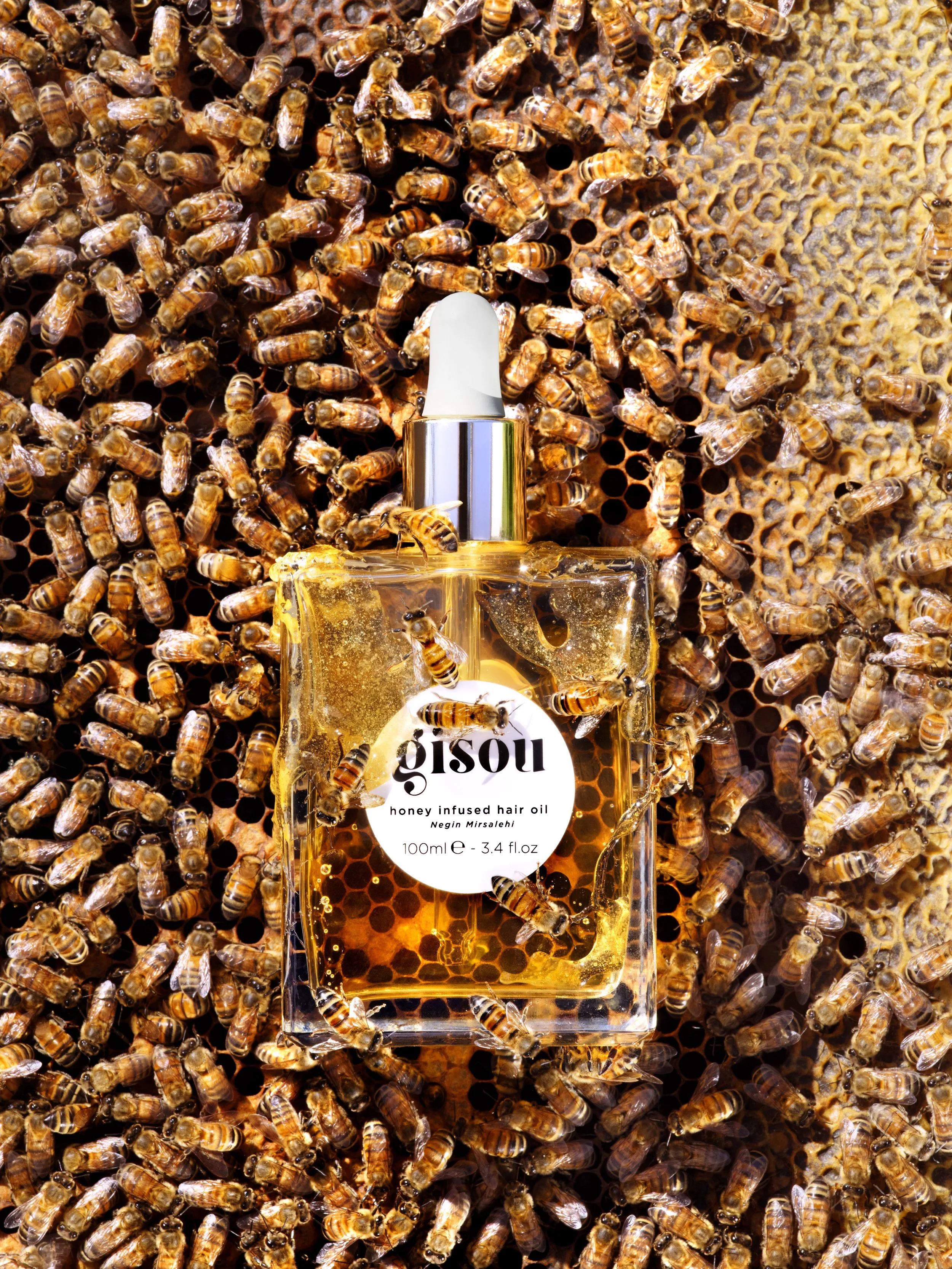 A honey infused hair oil bottle placed on a honeycomb surrounded by numerous bees.