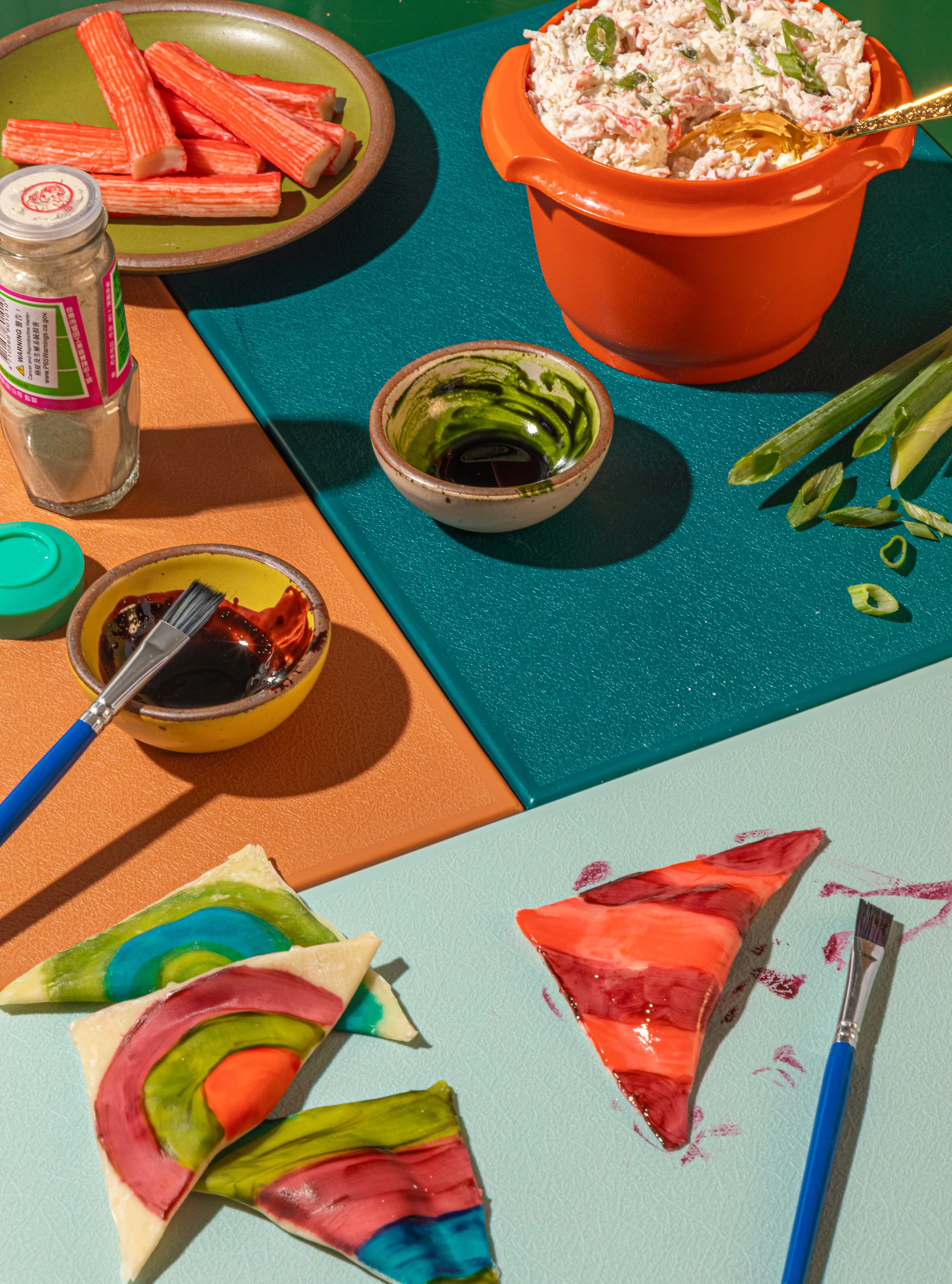 Colorful slices of fruit-shaped art on a white surface, including watermelon, kiwi, and watermelon slices, with a bubble tea and condiment bowls nearby.