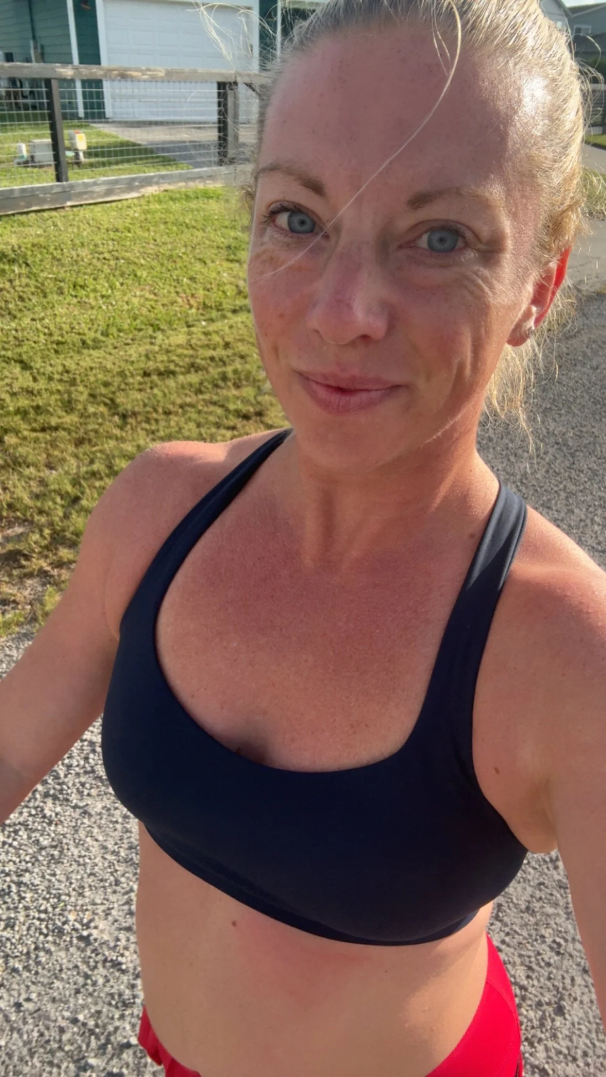 A woman with light skin and freckles, wearing a black sports bra and red shorts, outdoors during sunset.