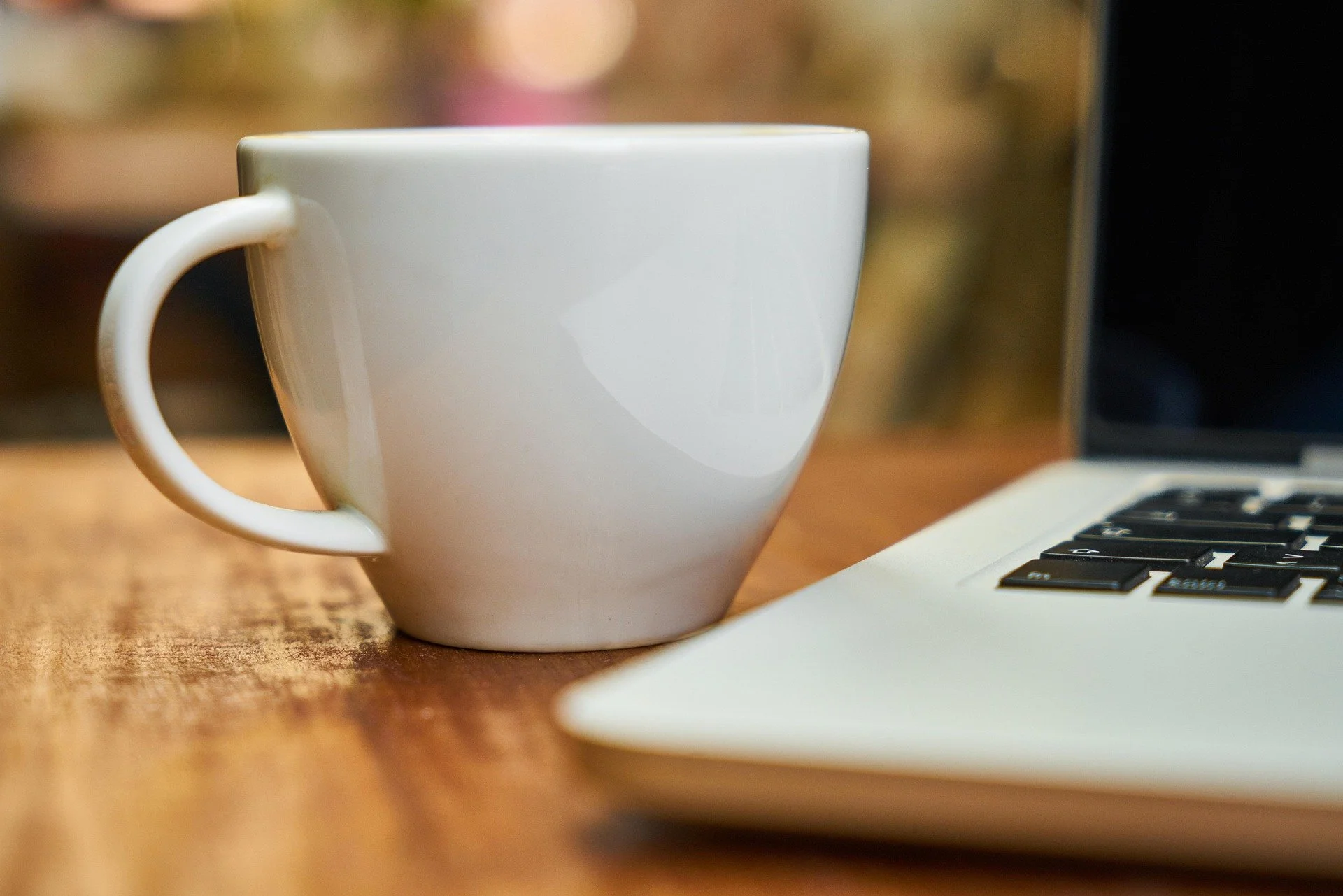 Close-up of a white coffee mug on a wooden table next to a laptop keyboard.